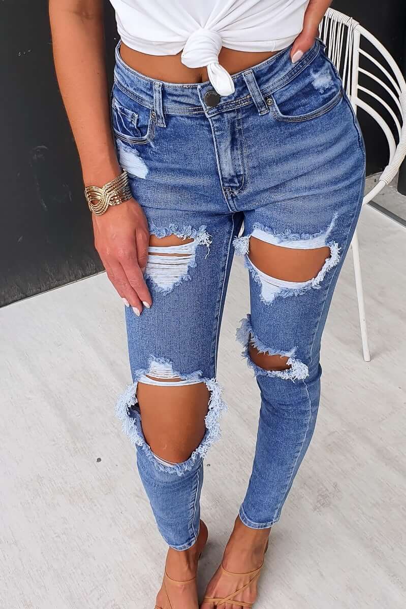 Model wearing Fletcher distressed denim jeans with mid-high waist, featuring rips and pockets, styled with a white top.