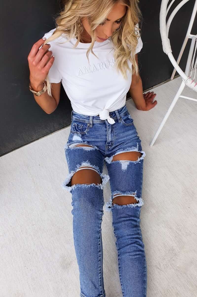 Model wearing Fletcher Jeans with distressed rips, paired with a white tee, showing mid-high waist fit and style.