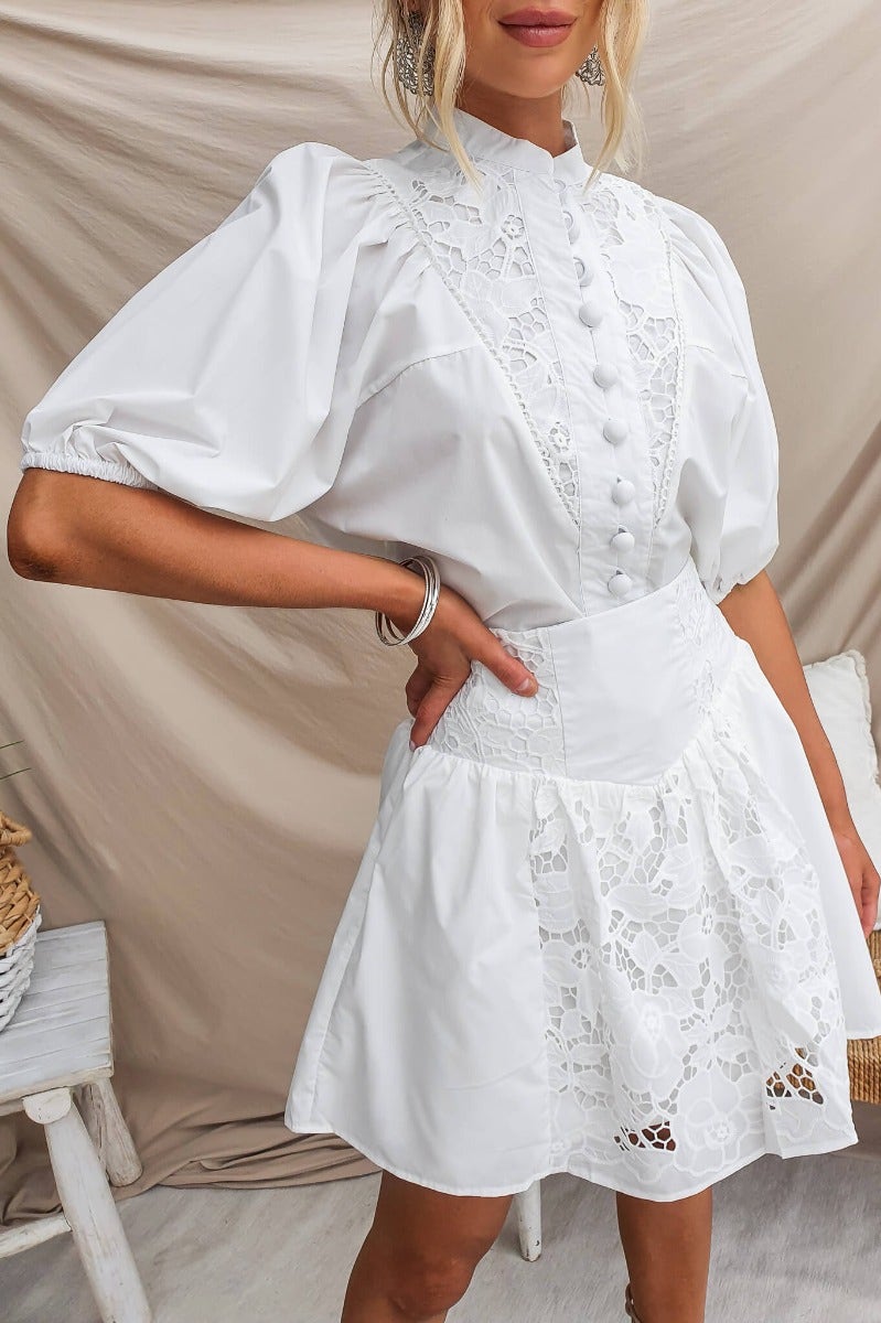 Model wearing a white dress with lace detailing and puff sleeves, styled for a chic summer look.