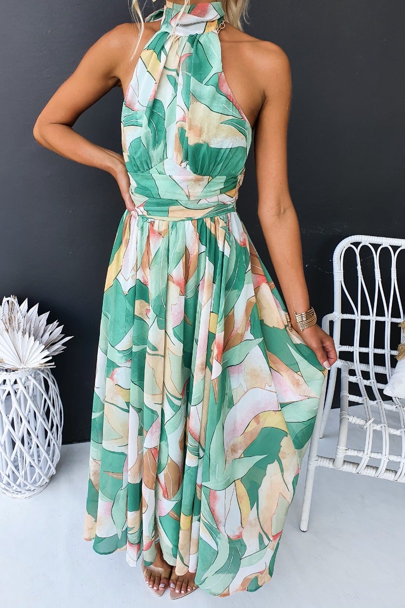 Floral print maxi dress with high tie neckline, featuring greenery and pastel colors, perfect for summer events.