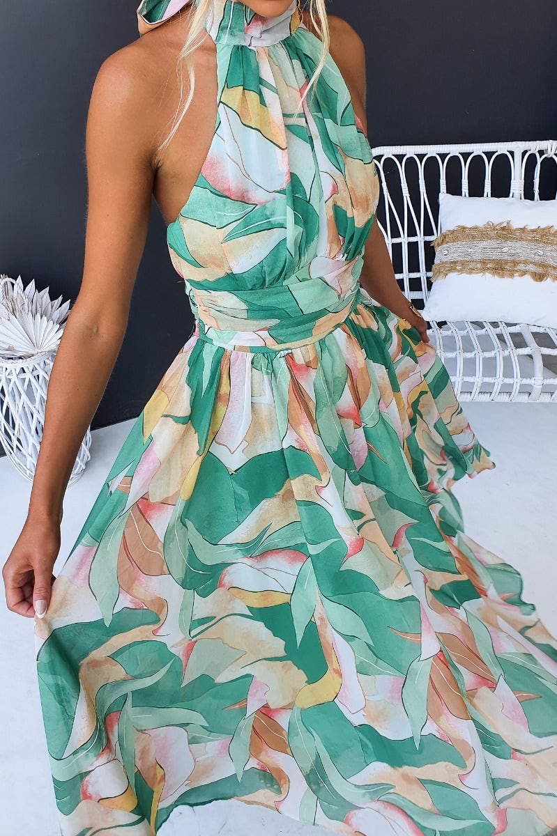 Model showcasing the Little Things Maxi Dress with a floral print and high tie neckline against a stylish backdrop.