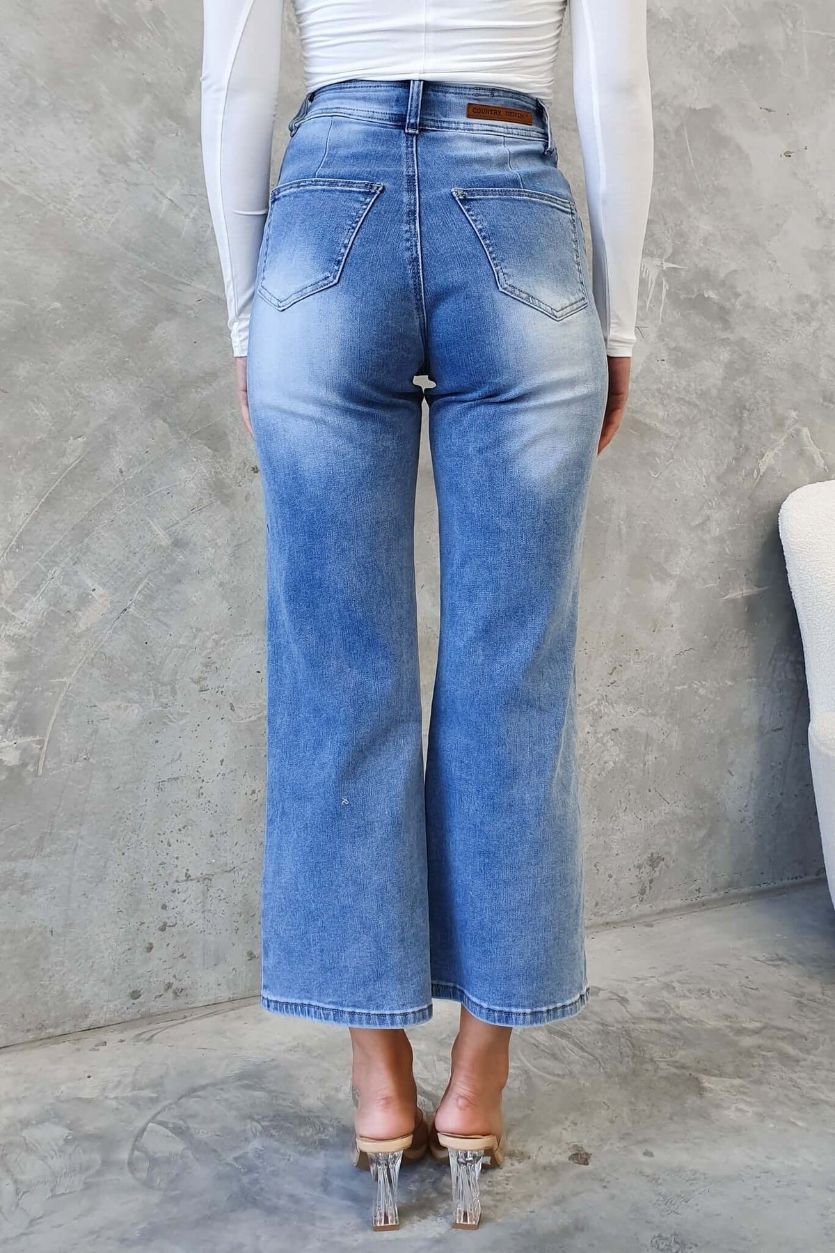 Back view of Blanca Jeans featuring a mid-high waist, wide legs, and back pockets on a model wearing clear heels.