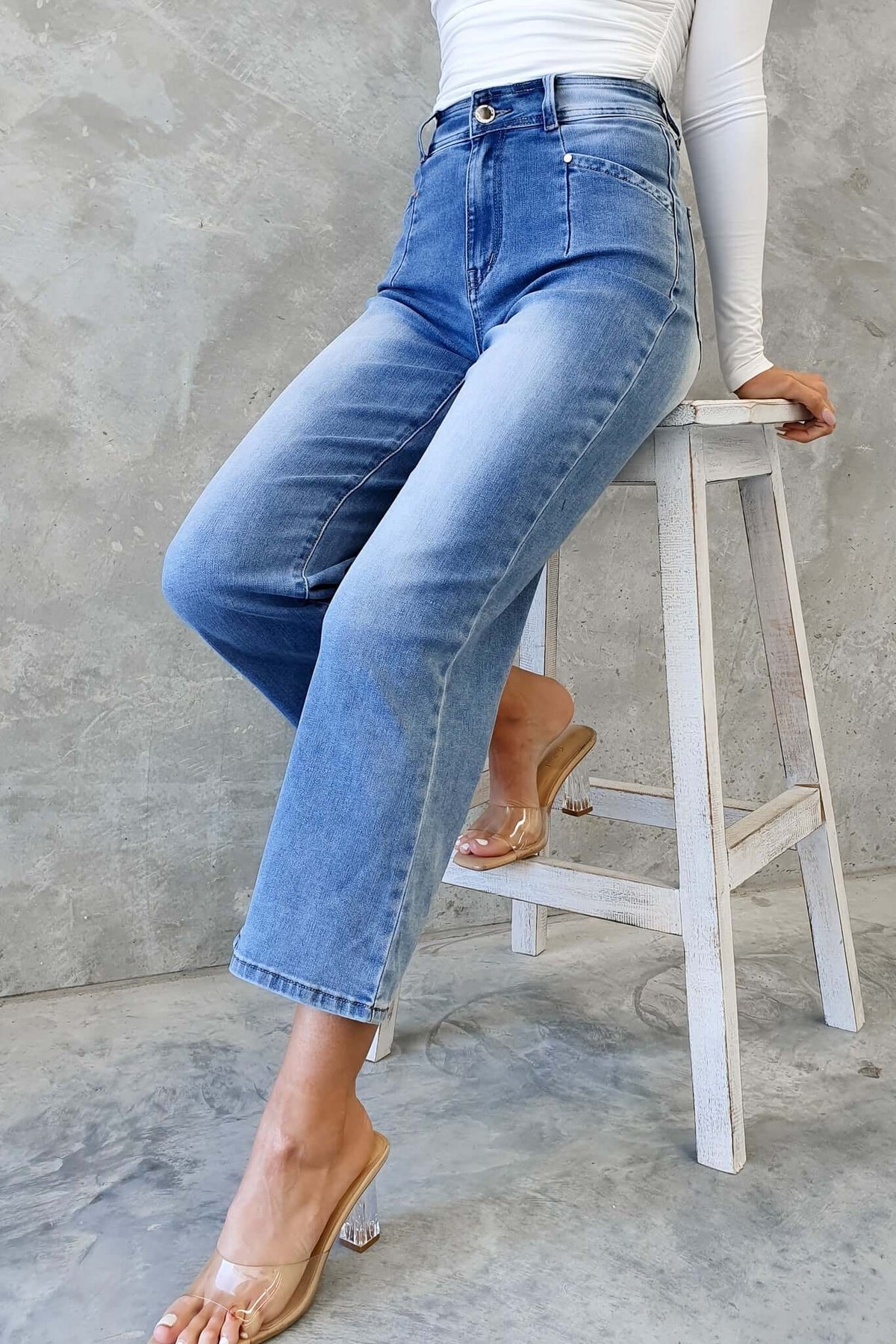 Blanca Jeans: mid-high waist denim jeans with wide legs, styled gracefully on a model sitting on a stool.