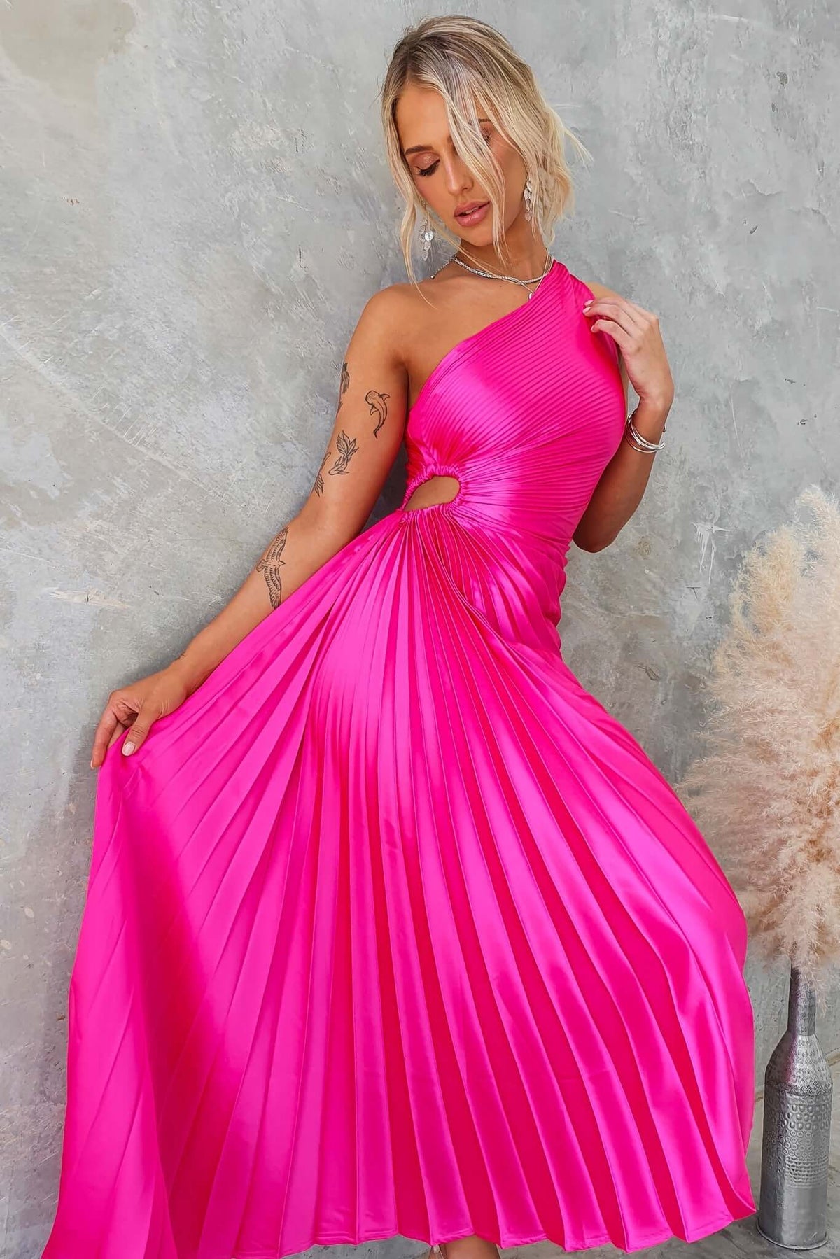 Model in a bright pink Olympia Maxi Dress featuring a one-shoulder neckline and cut-out waist, showcasing accordion pleats.