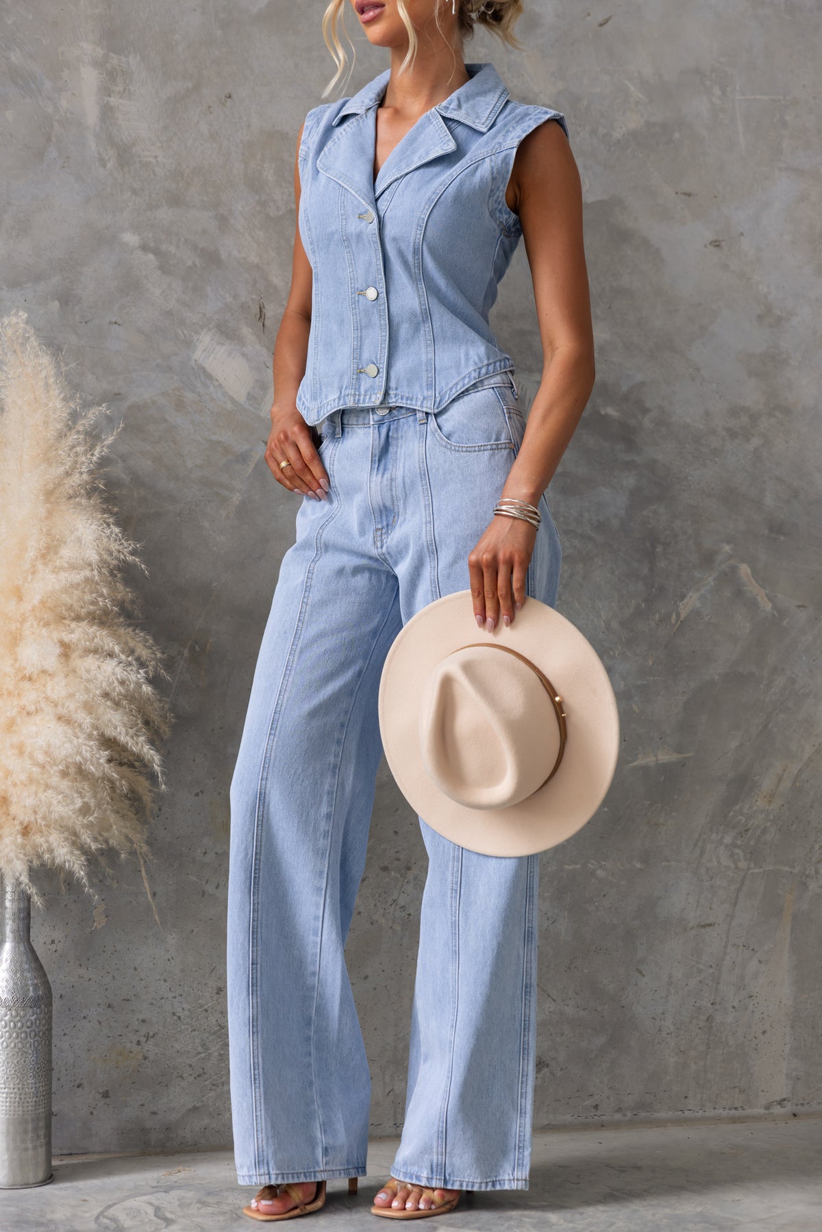 Model in light blue Billie Jeans with wide legs and a matching denim vest, holding a cream hat, chic summer outfit.