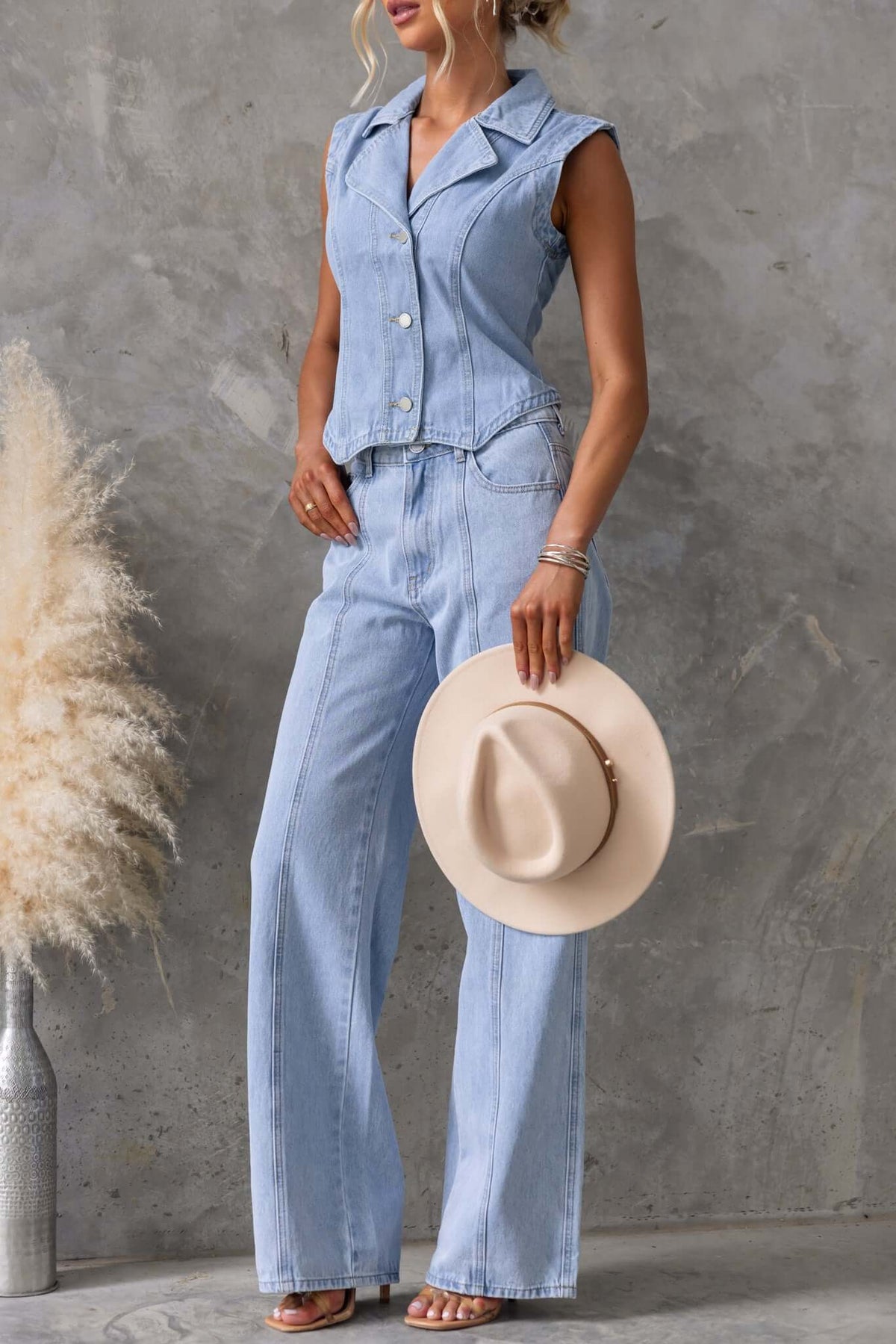 Model in light blue Billie Jeans with wide legs and a matching denim vest, holding a cream hat, chic summer outfit.