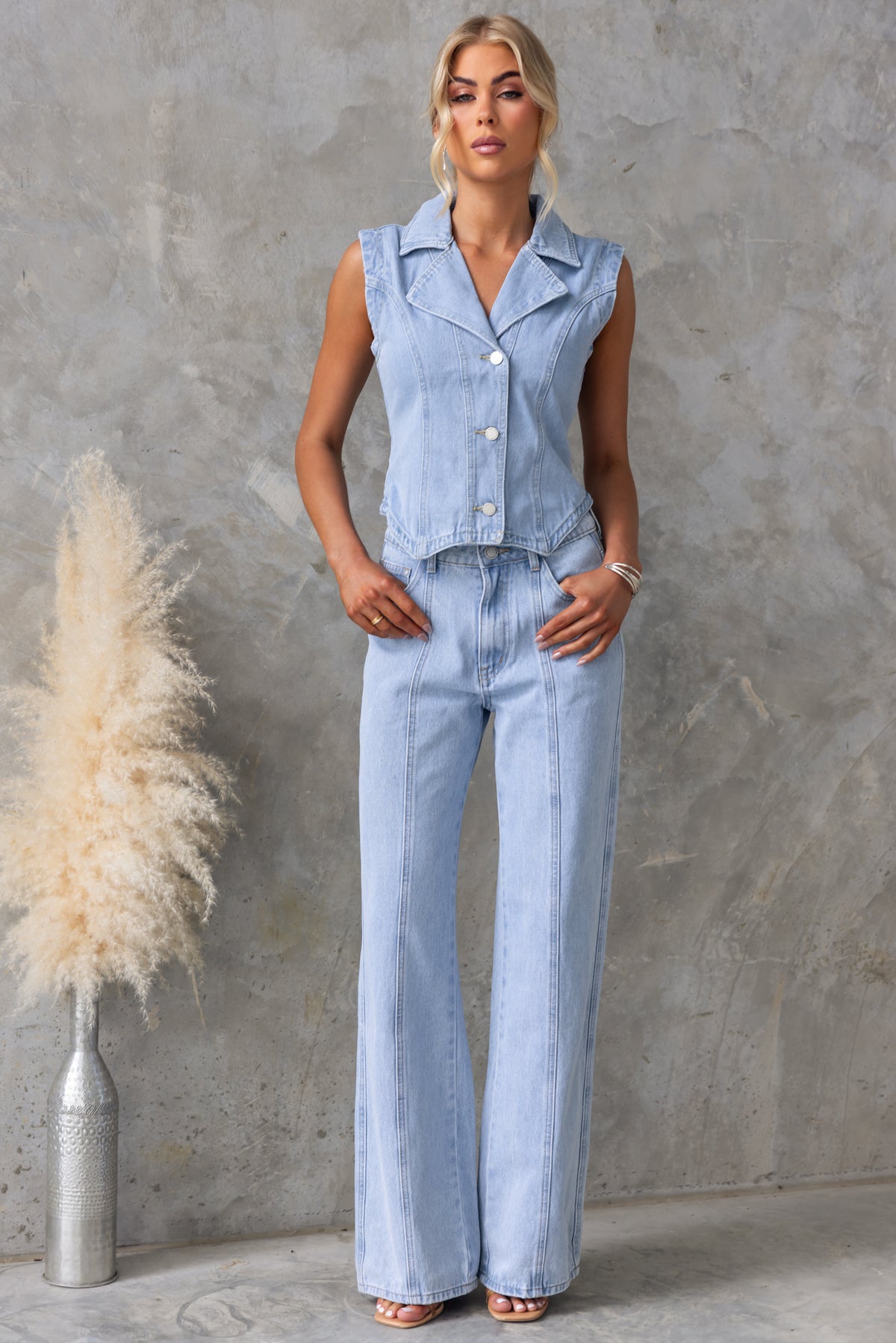 Model wearing Billie Jeans with a sleeveless denim top and wide-leg jeans, styled against a textured wall.