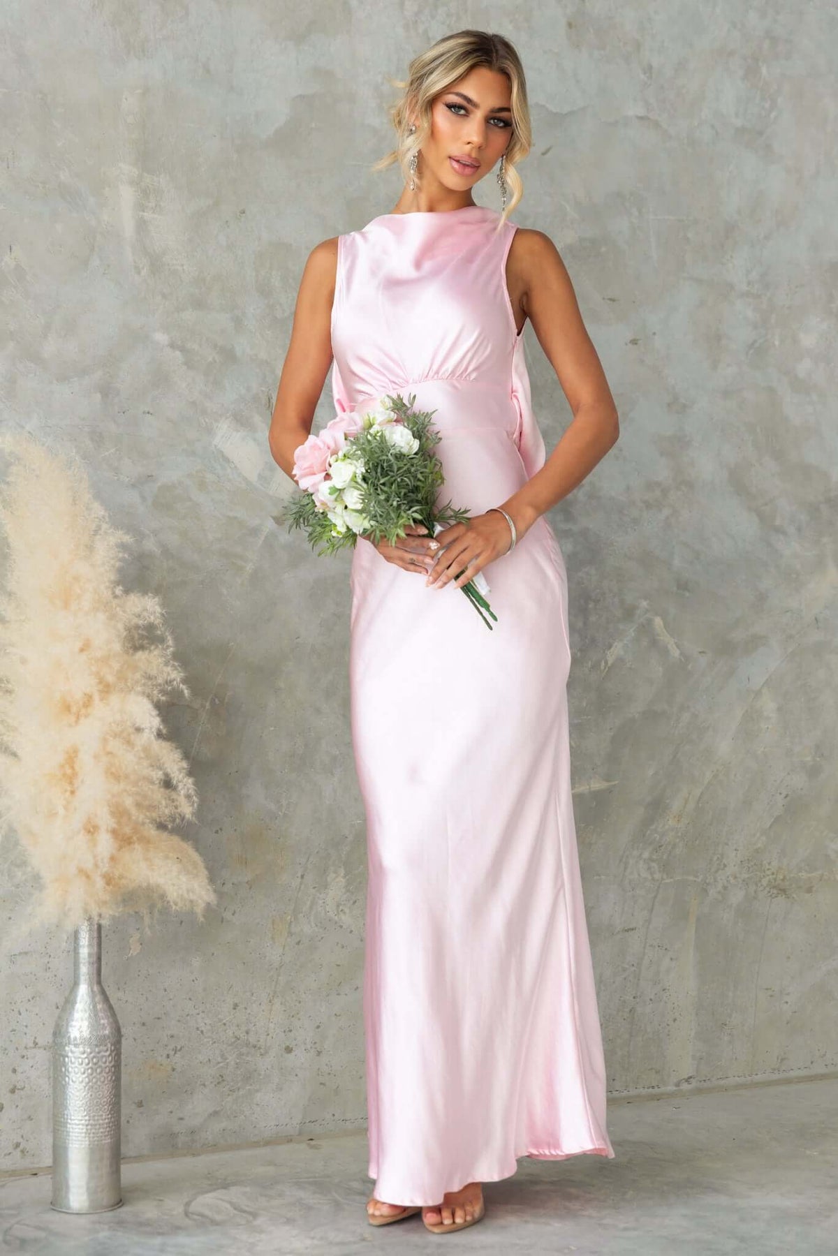 Silvia Maxi Dress in pink satin with boat neckline, draping back, and bouquet, styled for a bridal occasion.