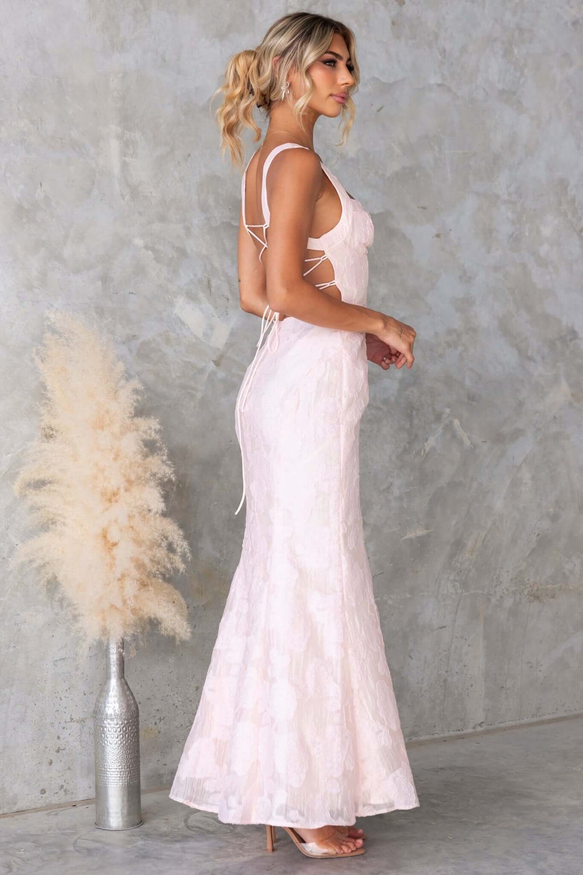 Side view of the Remma Maxi Dress featuring a lace-up back, textured material, and slight fishtail hem.