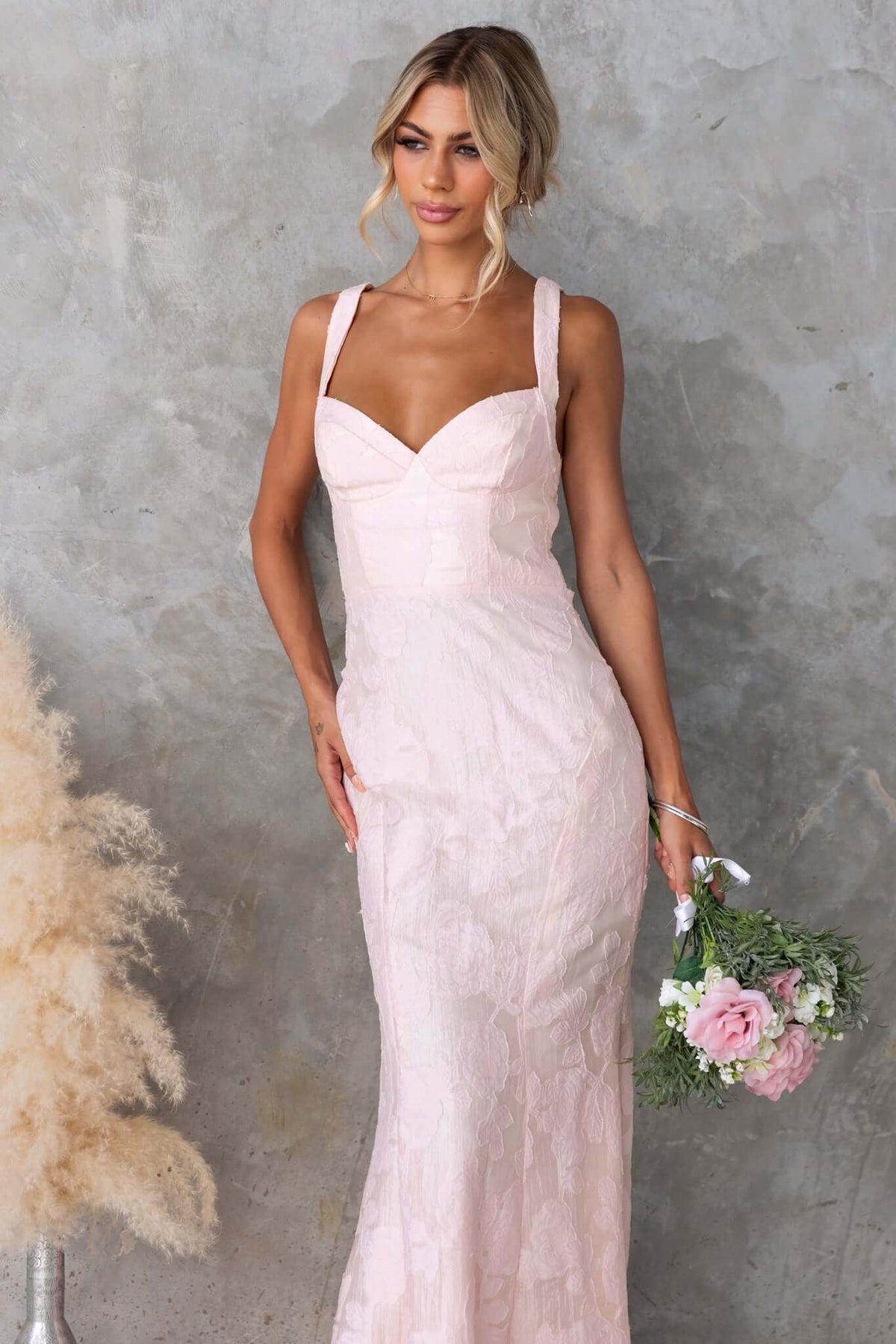 Remma Maxi Dress in light pink lace, featuring a lace-up back, slight fishtail hem, and textured fabric, perfect for special occasions.