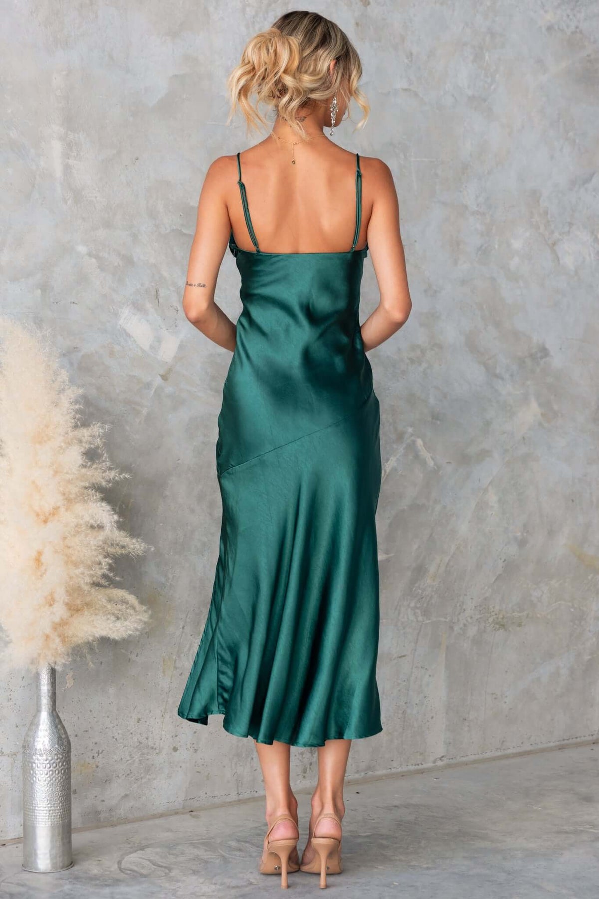 Back view of the Brighton Midi Dress in emerald green satin with adjustable straps and a flowing split.