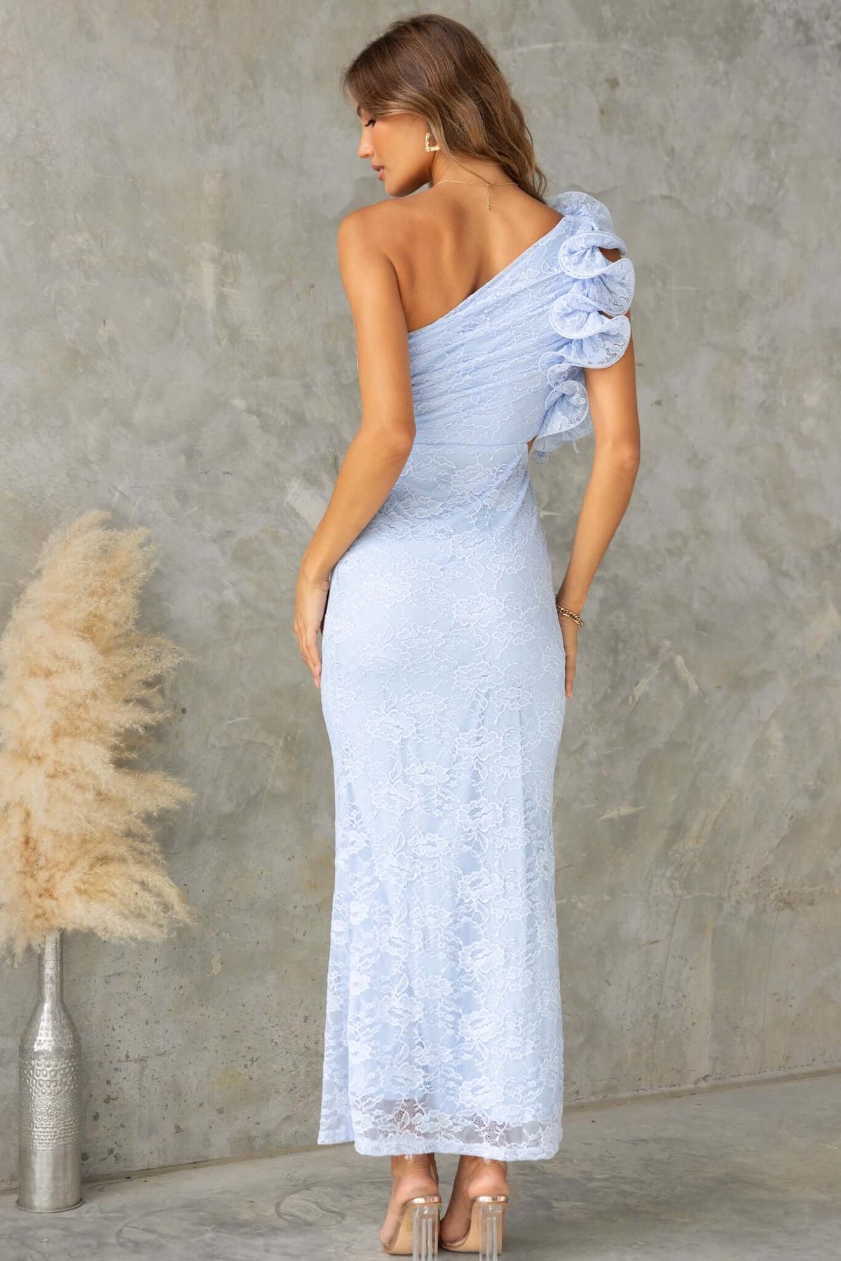 Rear view of the Meriden Maxi Dress, a one-shoulder lace gown with a cutout waist and fluted detailing in light blue.