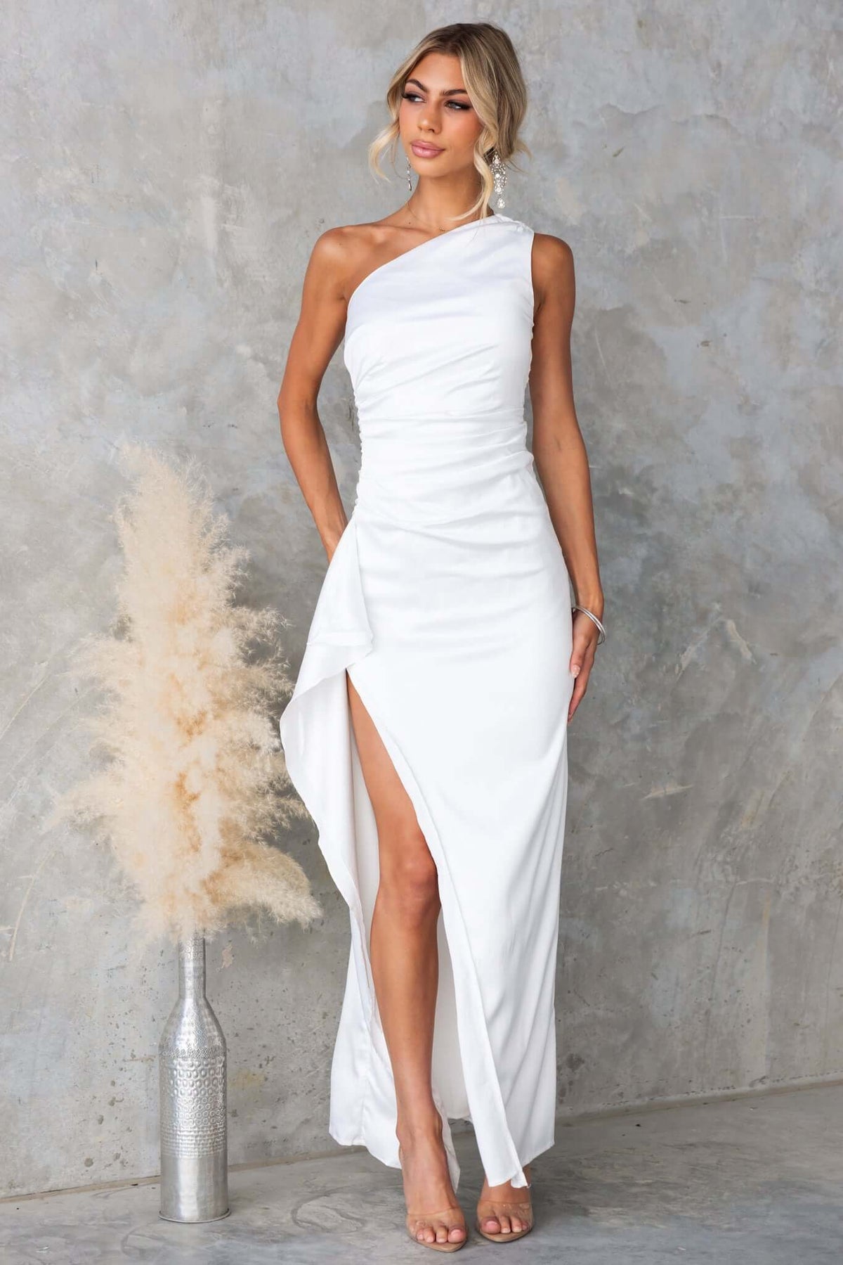 Dimmi Maxi Dress in white satin, featuring one-shoulder neckline, side slit, and asymmetrical hemline with ruffle trim.