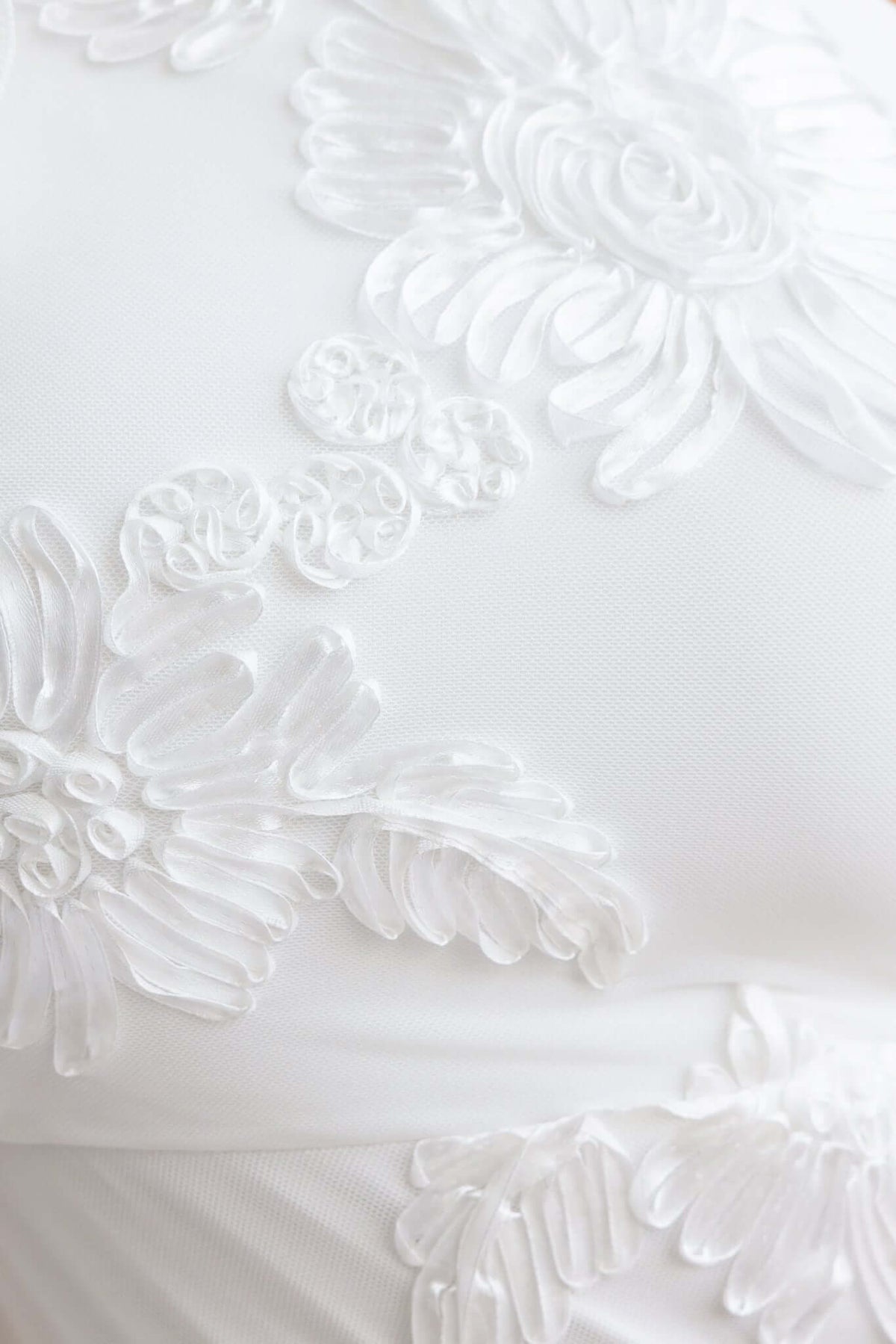 Close-up of embroidered floral details on a white mesh fabric of a maxi dress.