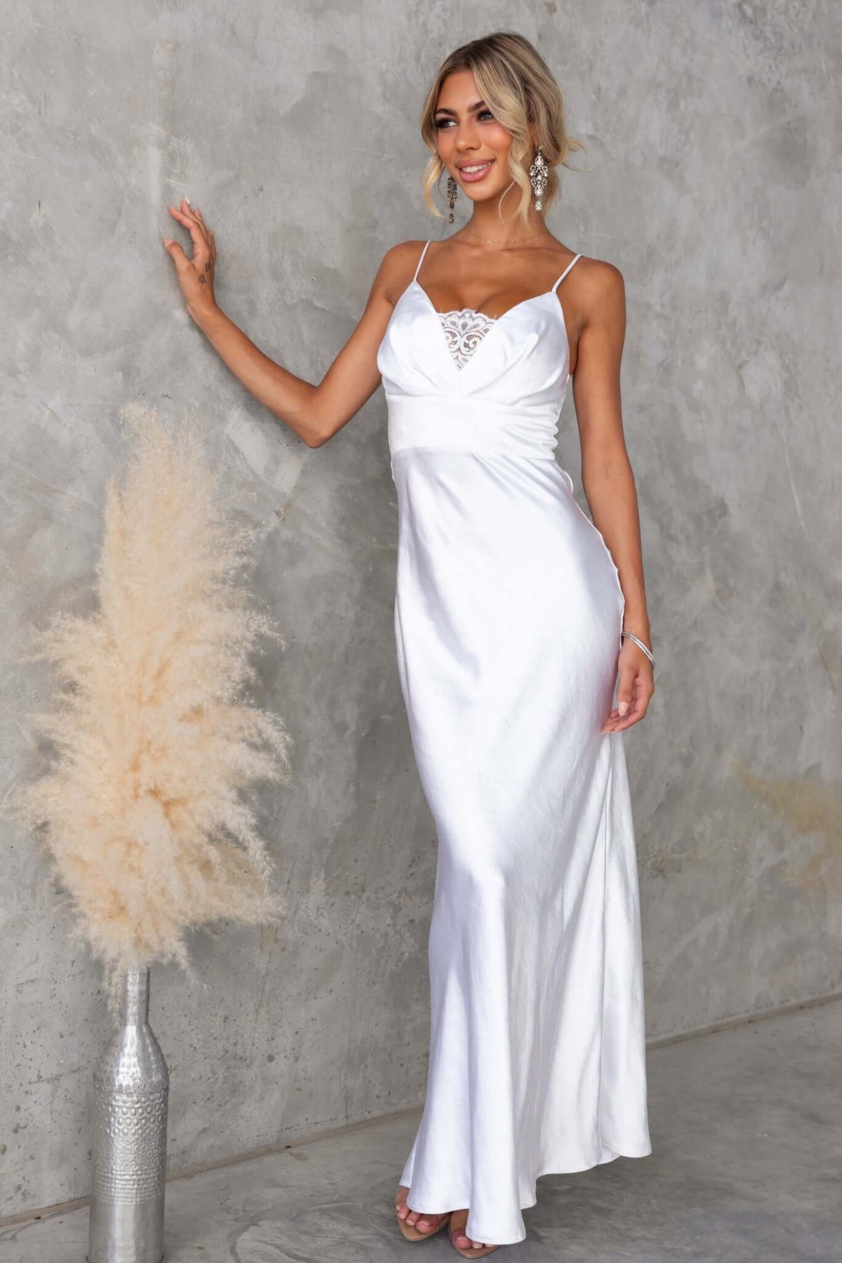 Model in a Maricia maxi dress, showcasing adjustable straps and lace panel detail against a textured wall.