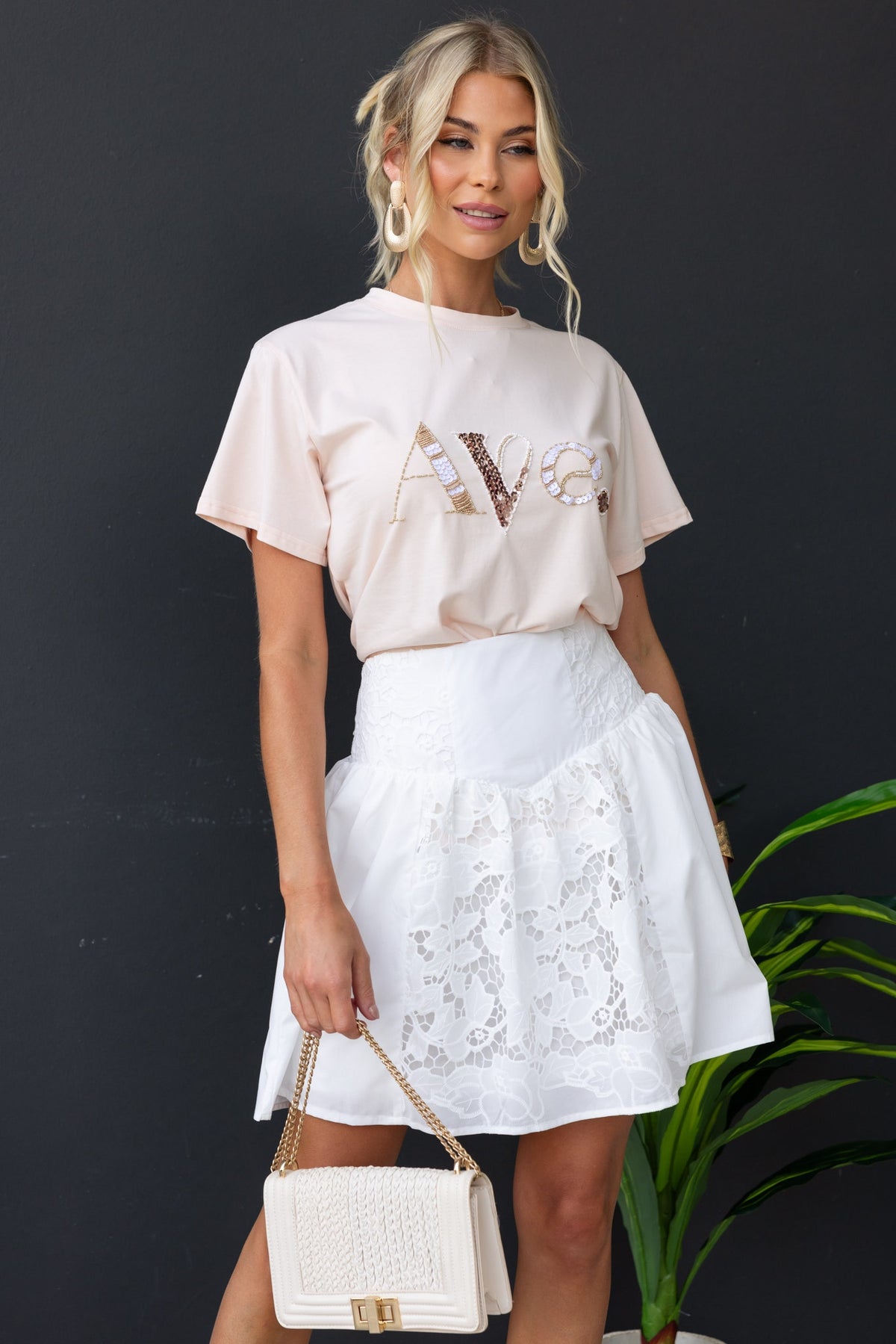 Model wearing a fancy white cotton blend skirt with Anglasie detailing paired with a pink top and a stylish handbag.