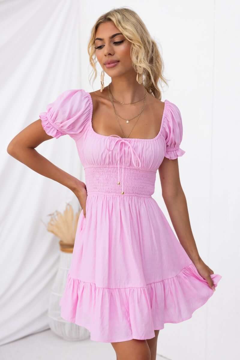 Model wearing a pink Love In Motion Dress with round neckline and tie detail, featuring elastic waistband and sleeves.
