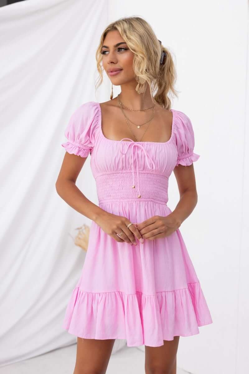 Love In Motion Dress in pink, featuring elastic neckline, tie detail, and flared skirt.