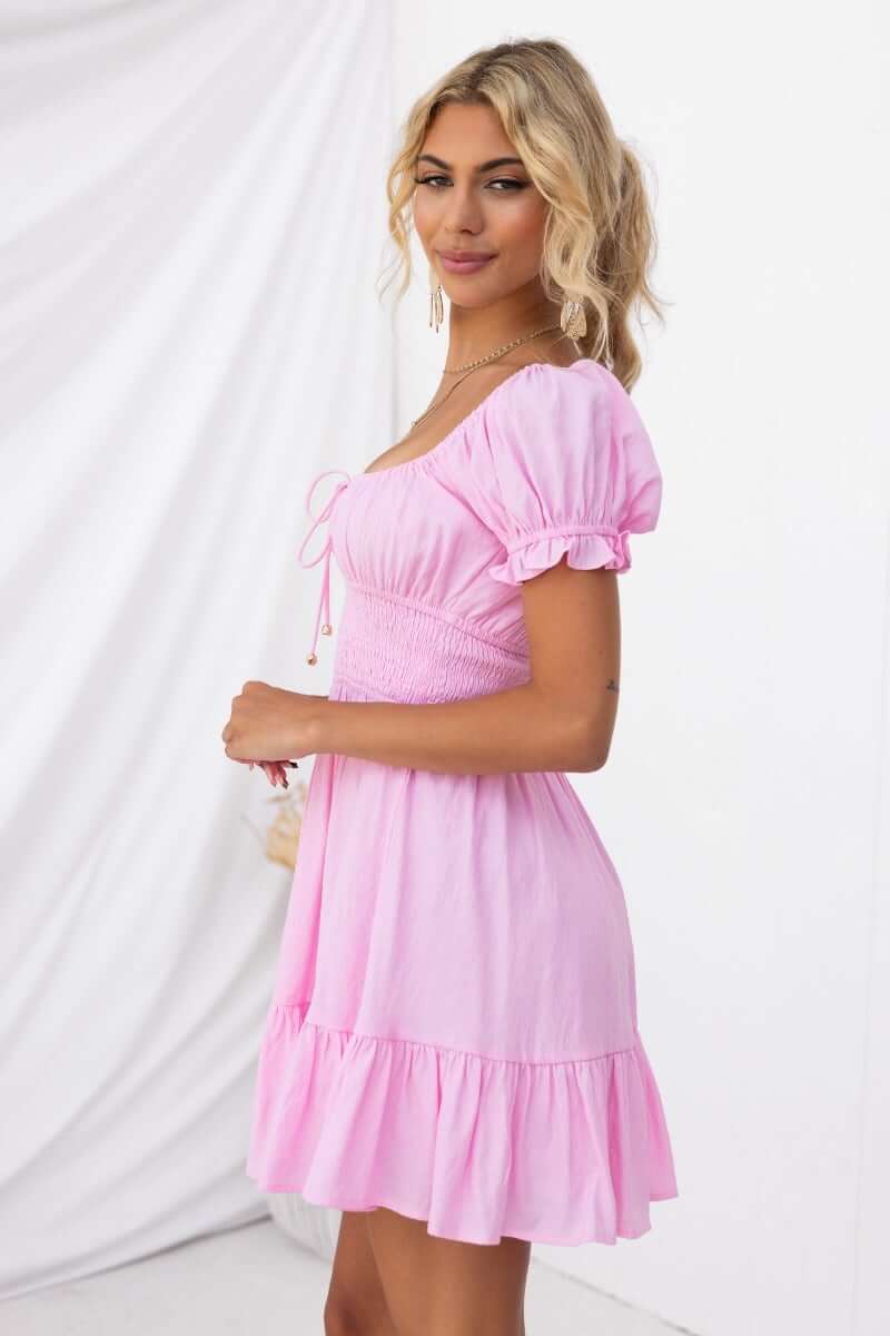 Side view of a woman wearing a pink Love In Motion Dress with round neckline and elastic details.