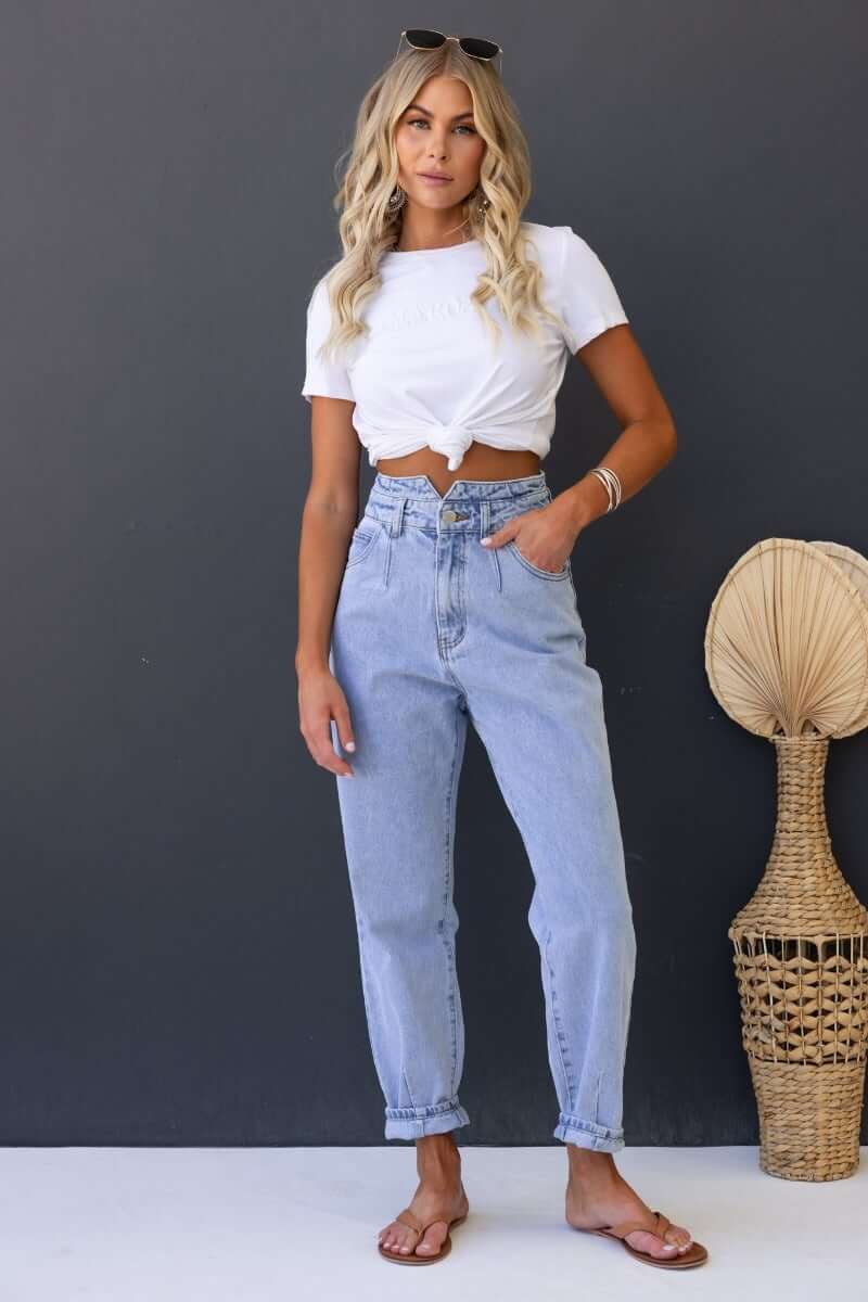 Woman wearing Shaylan Mom Jeans with a white knotted shirt, showcasing mid-high waist fit and wide legs.