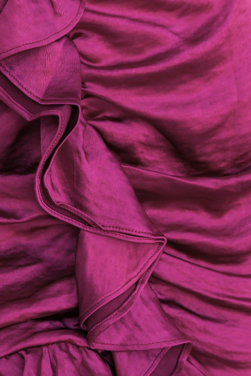 Close-up of ruffled trim on a satin fabric in vibrant magenta, showcasing texture and elegance.
