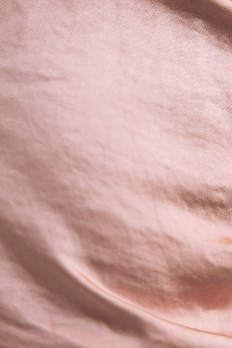 Close-up of smooth satin fabric in soft pink color, showcasing its gentle texture and sheen.