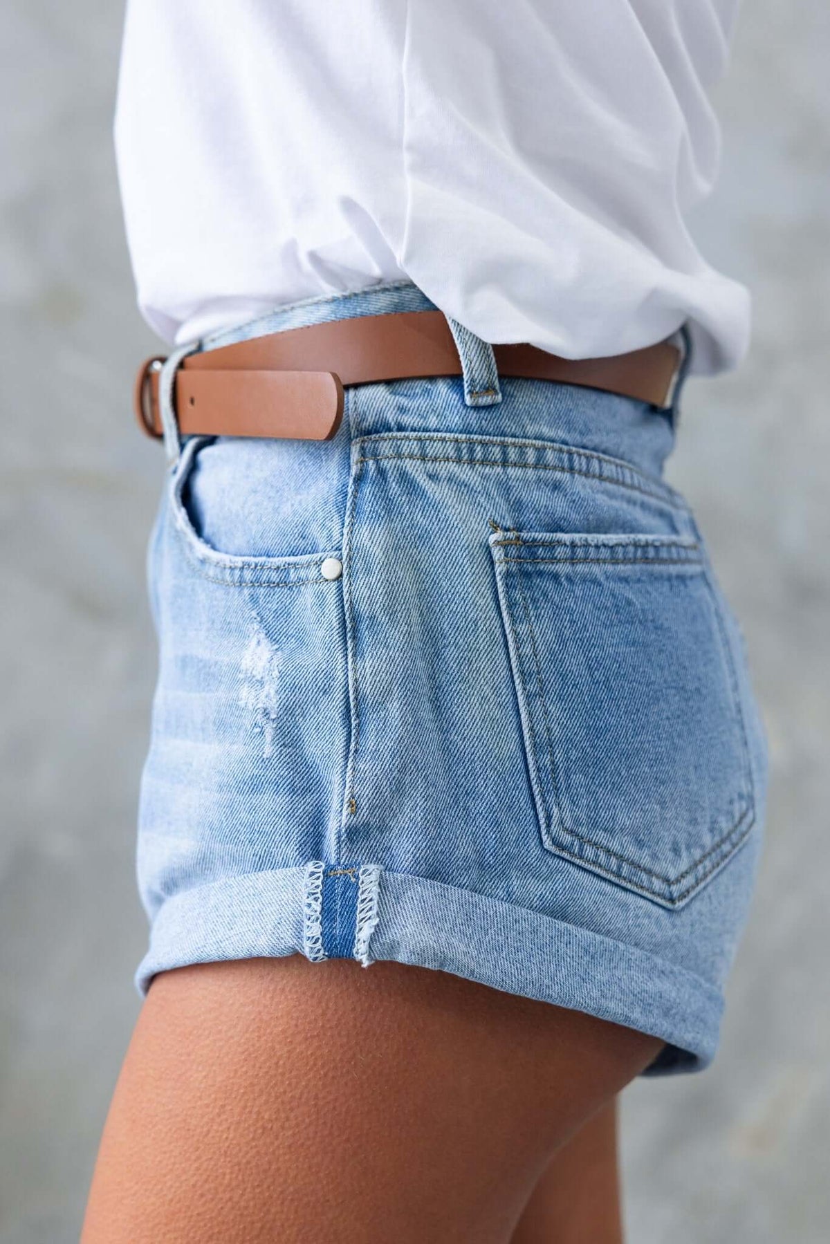 Kim Denim Shorts featuring a mid-high waist, distressed detailing, and pockets, styled with a brown belt.