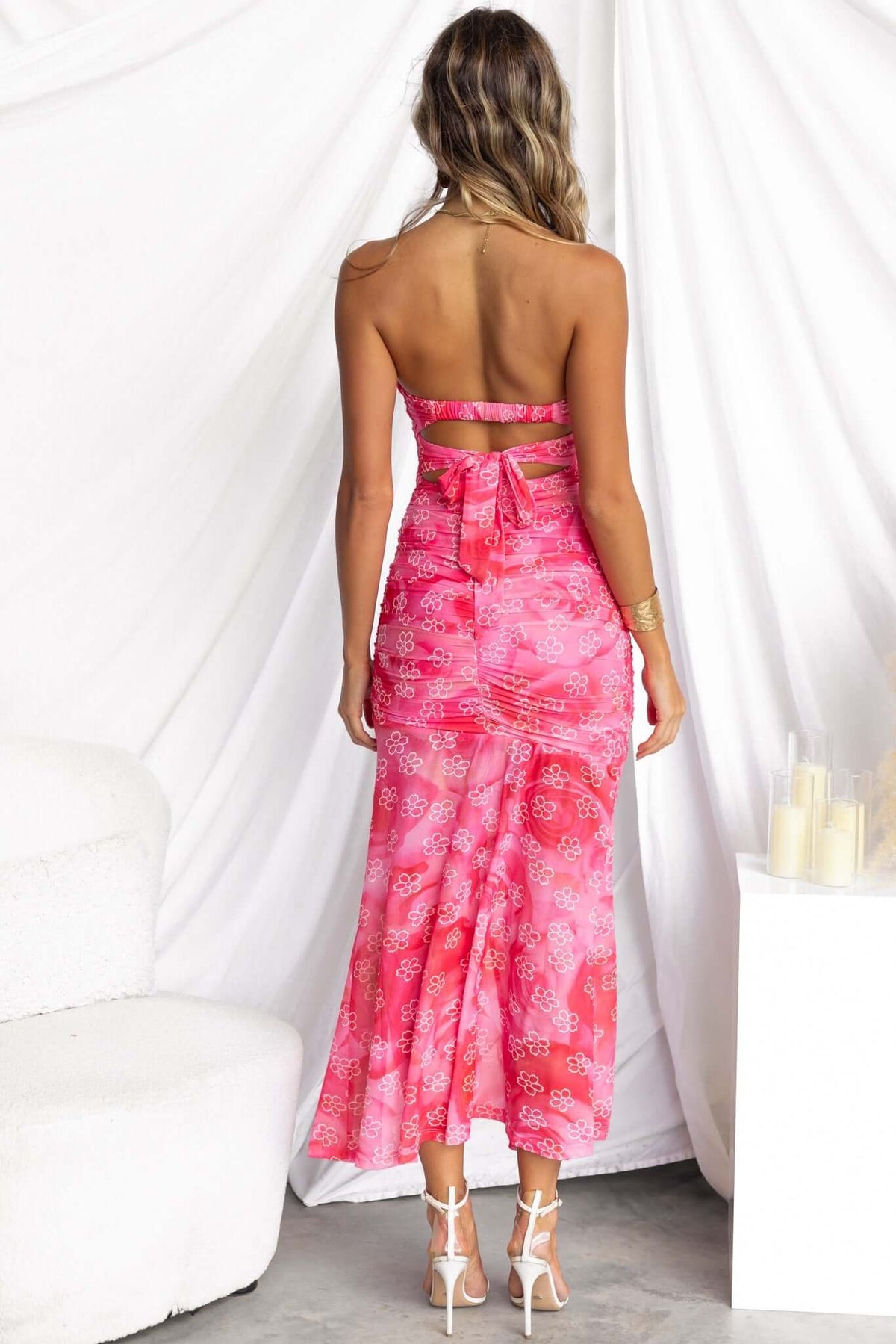 Back view of a woman in a strapless pink midi dress with floral patterns and a split skirt.
