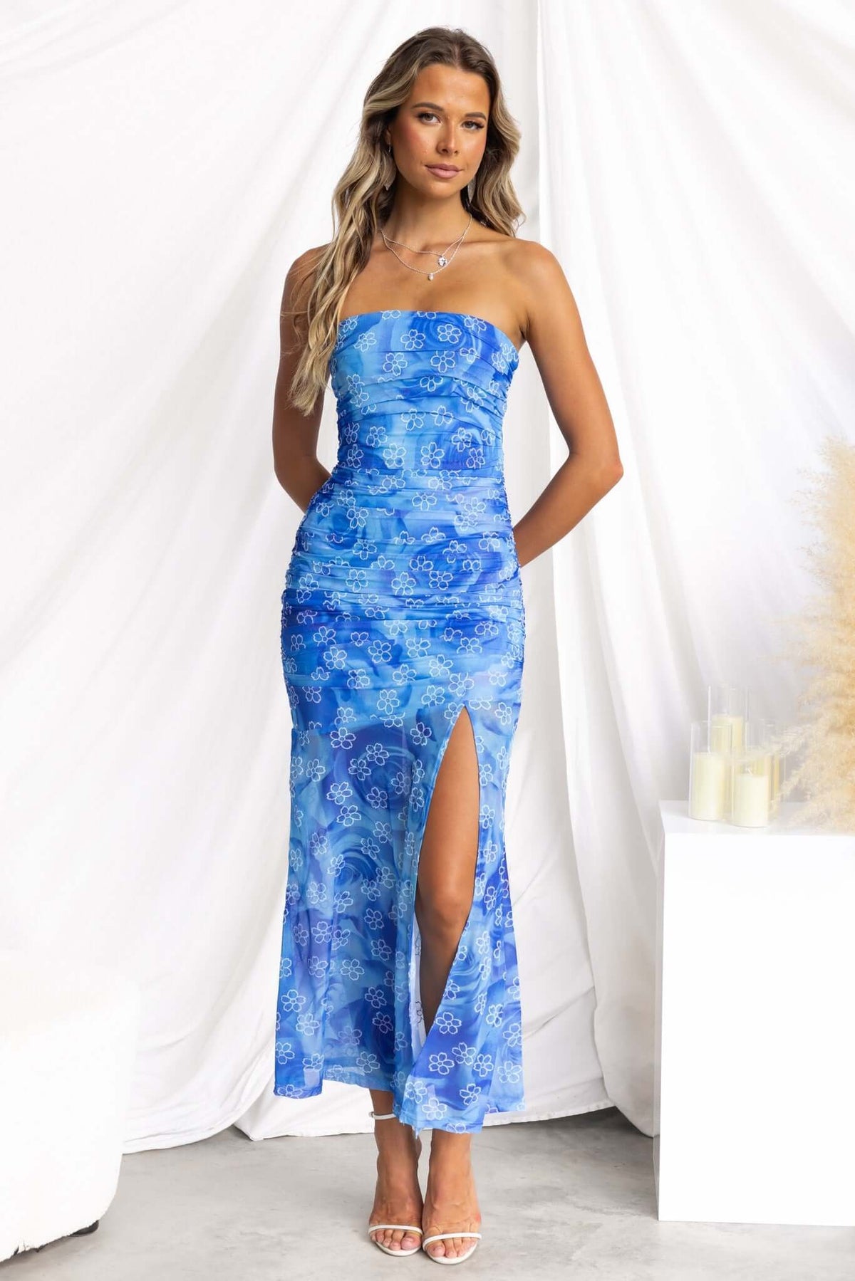 Model wearing a blue strapless Blomma Midi Dress with a front split and floral pattern, styled elegantly.