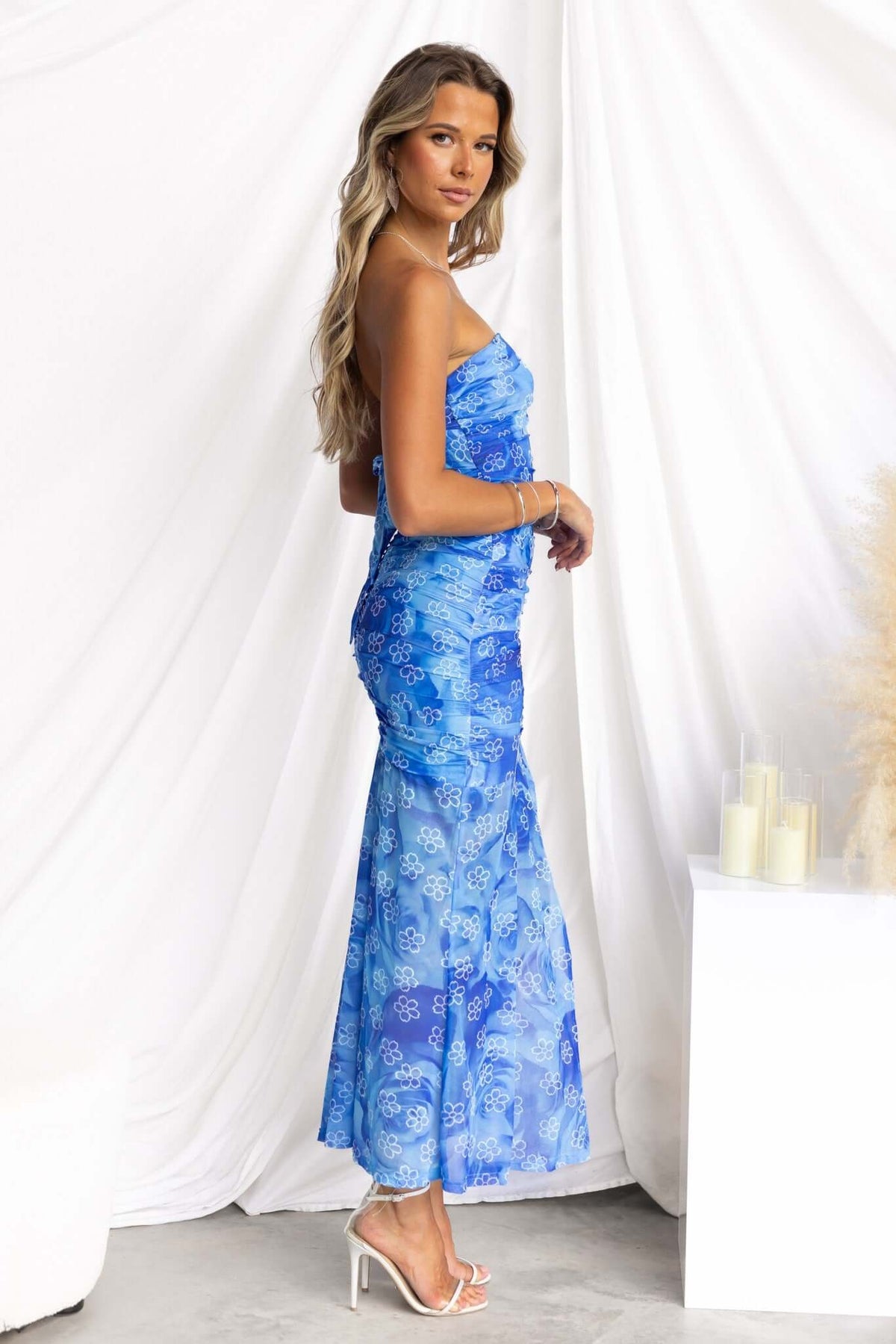 Model wearing a strapless Blomma Midi Dress in blue mesh with floral patterns, showcasing an elegant silhouette.