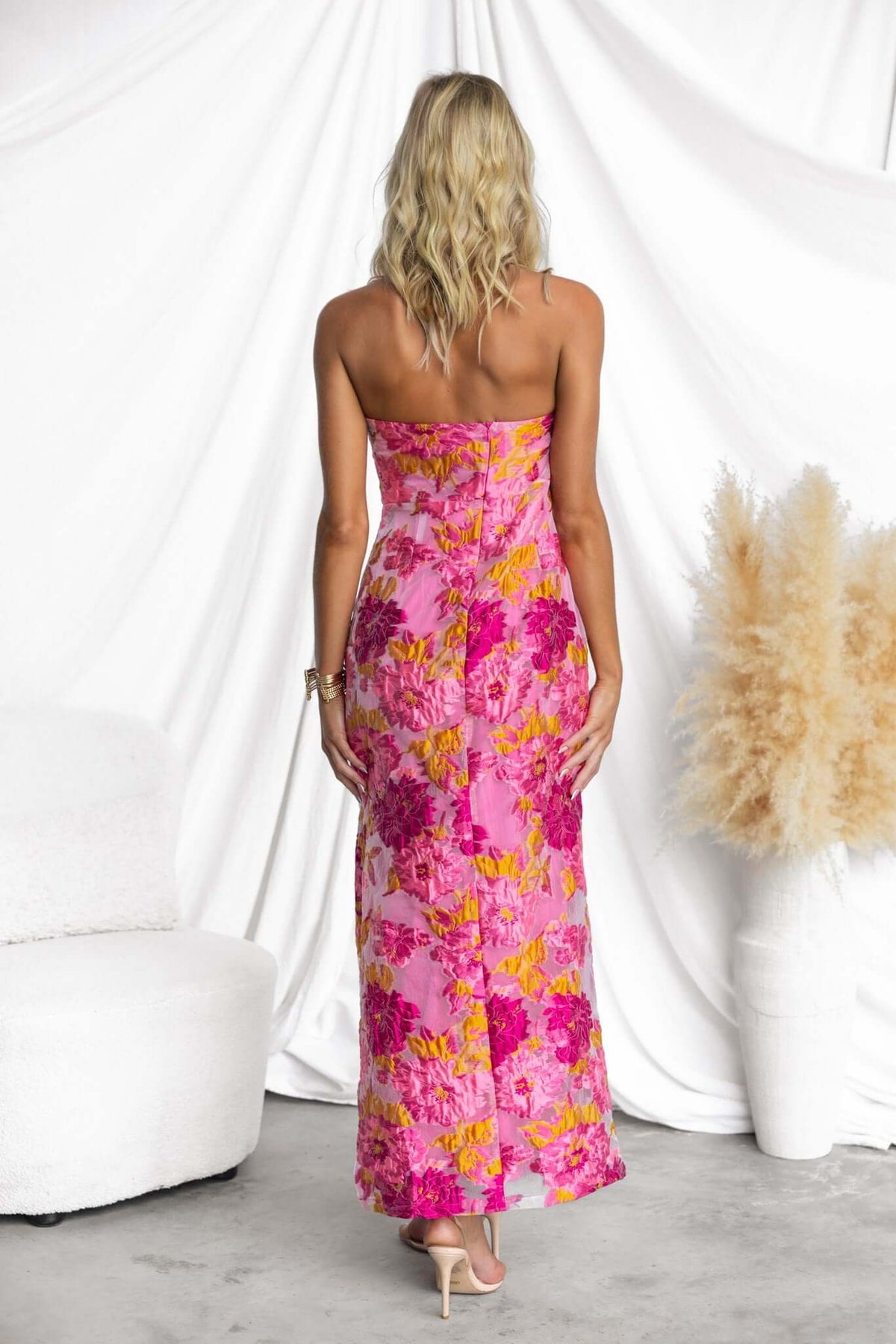 Back view of a woman in a floral print Kamryn Maxi Dress, featuring a strapless design and vibrant pink hues.