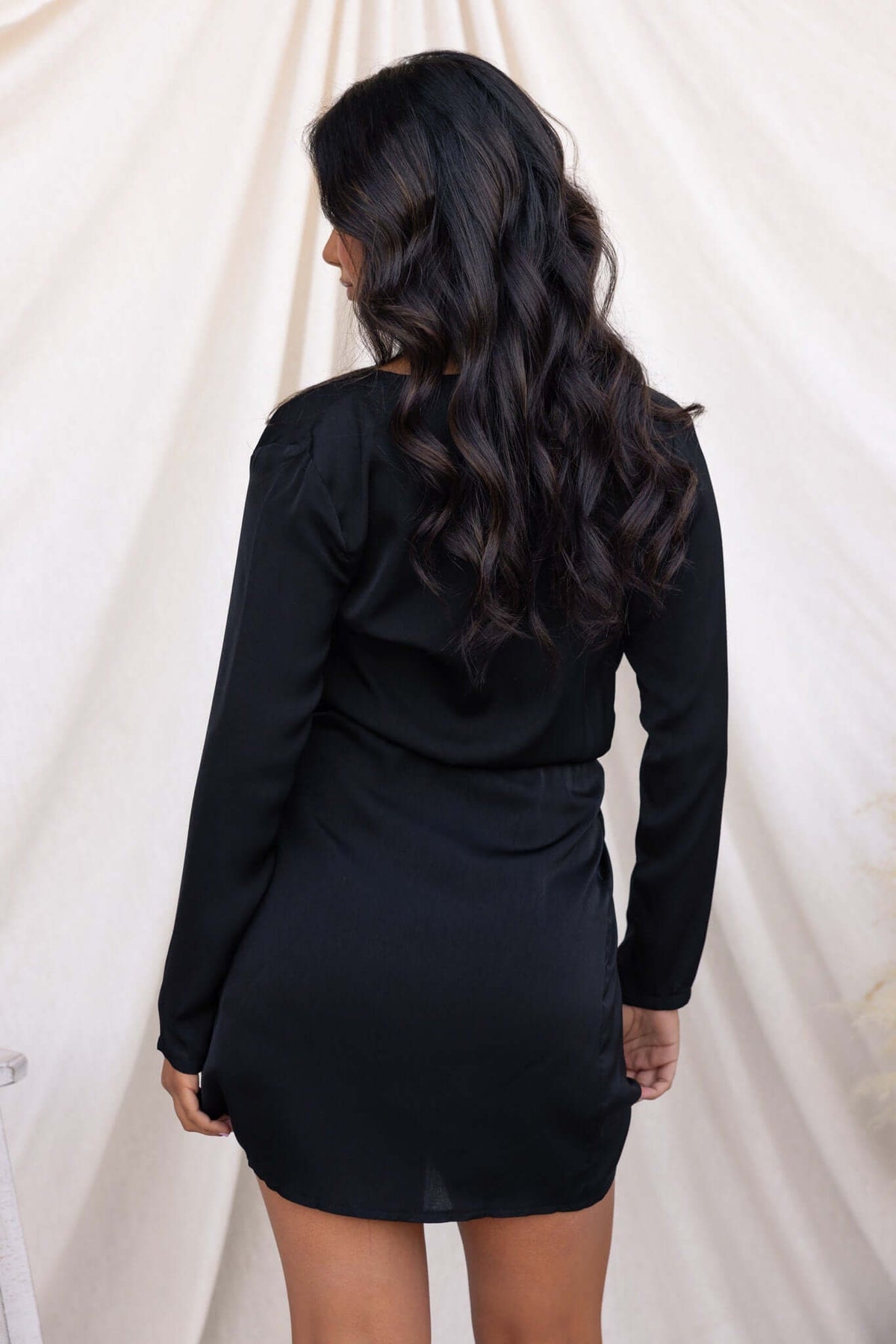 Back view of a model wearing a sleek black Miku Dress with long sleeves and V-neckline.