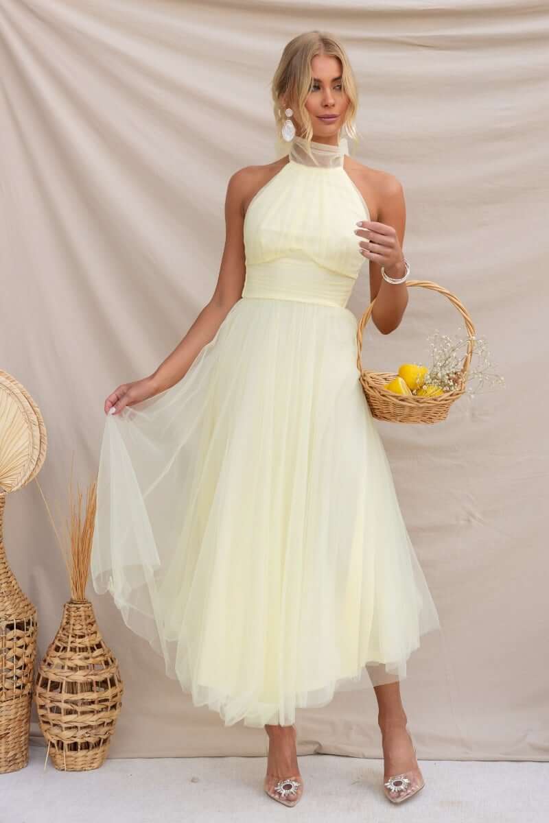 Model wearing a Love Lane Maxi Dress in soft yellow, featuring a halter neckline and tulle skirt.
