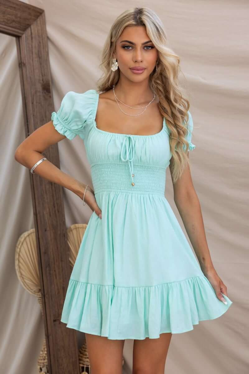 Love In Motion Dress in mint green with round neckline, tie detail, elastic waist, and short puff sleeves.