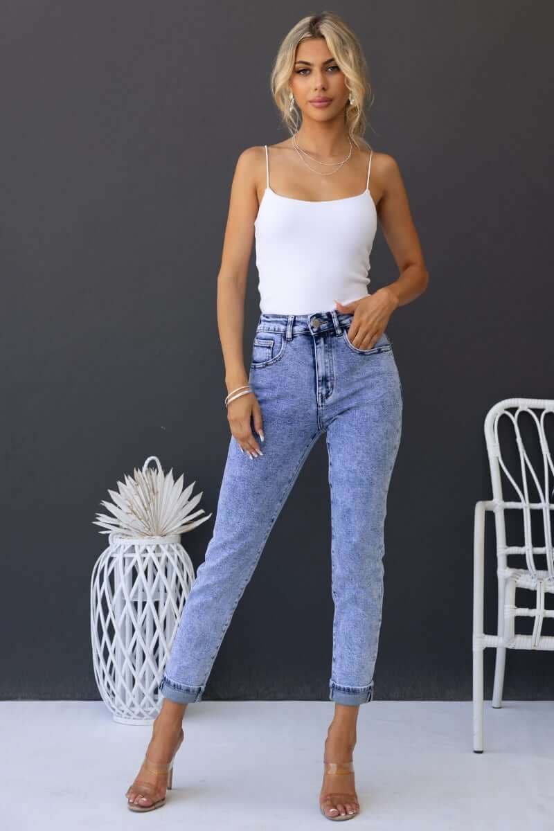 Woman modeling Hush Mom Jeans with mid-high waist, light wash denim, paired with a white tank top and stylish heels.