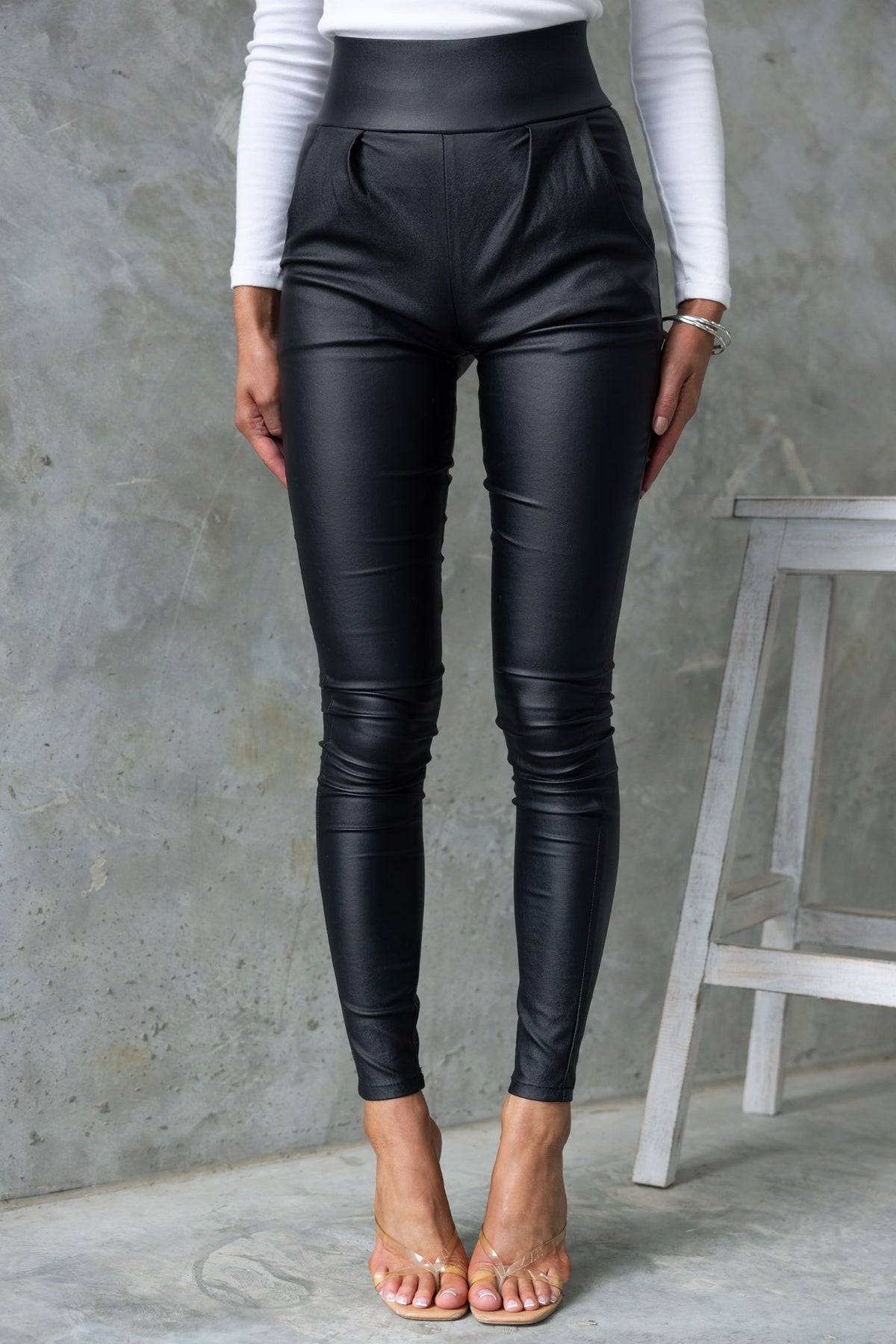High-waisted black faux leather Reece Pants with front pockets and stretchy material, styled for a modern look.
