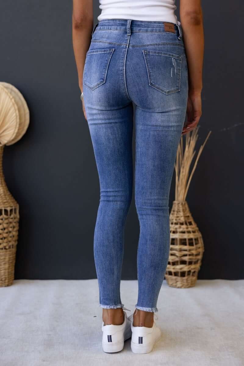 Back view of Qilli distressed denim jeans with raw hem and pockets, featuring a standard fit and stretchy material.