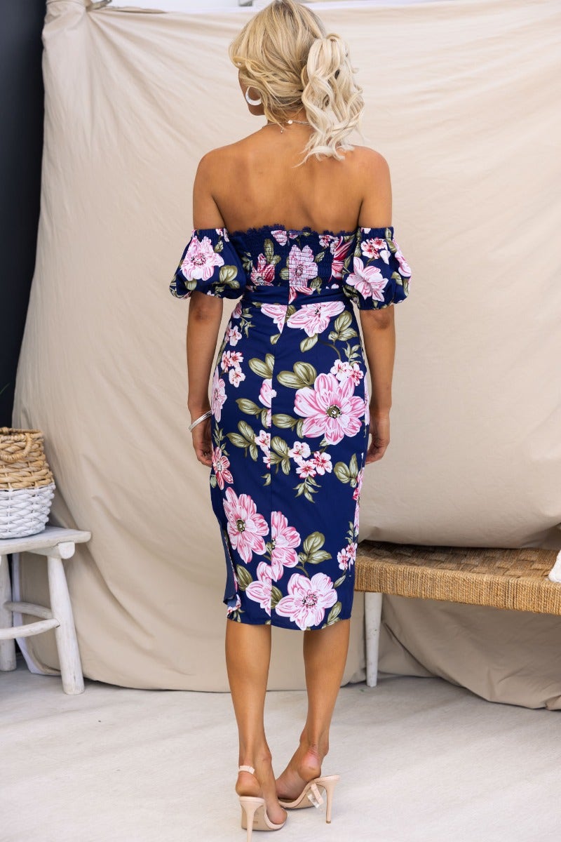 Back view of a navy floral midi dress with off-shoulder neckline and side split, styled with heels.
