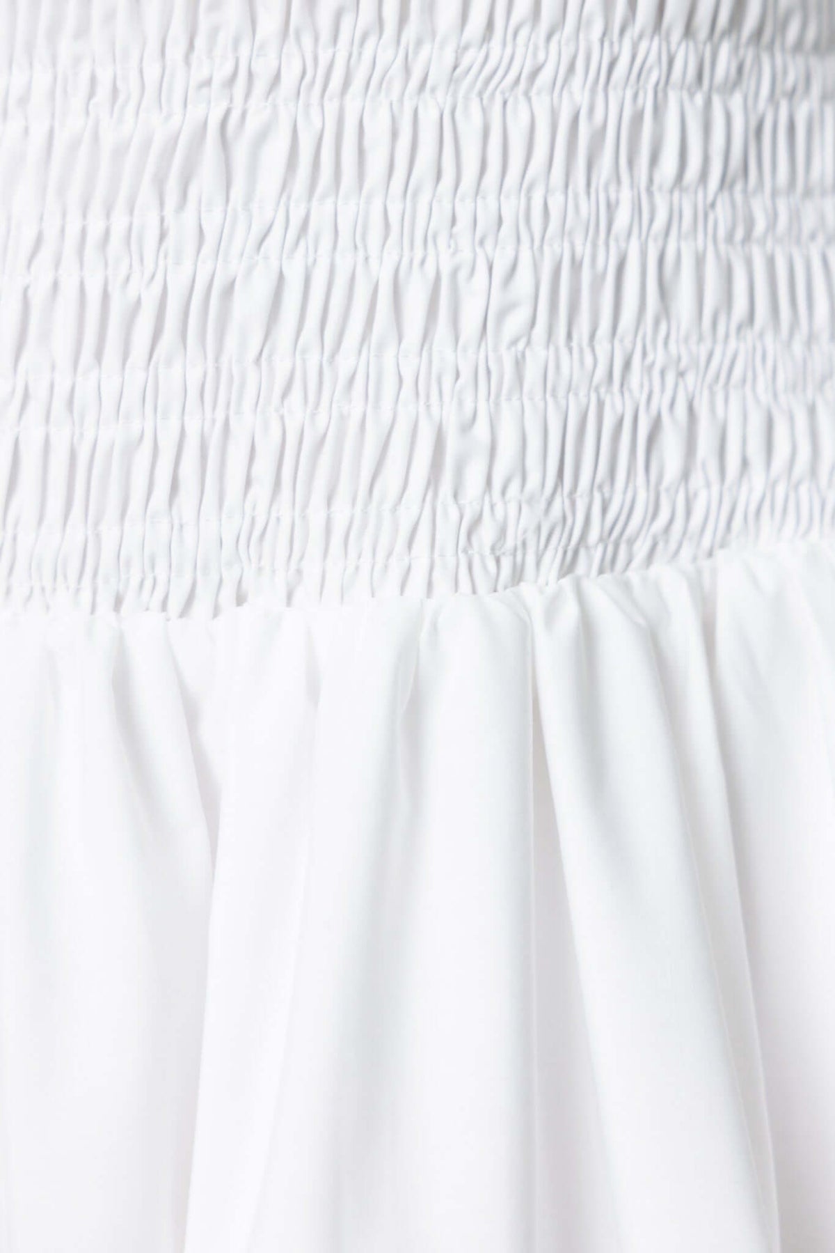 Close-up of the elastic bodice and flowing fabric of a strapless white midi dress.