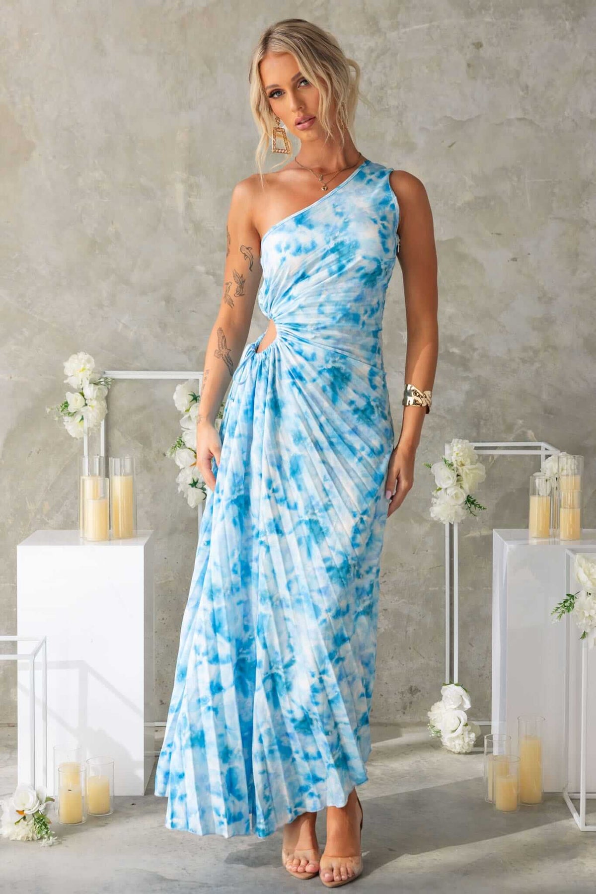 Tejano maxi dress features one-shoulder neckline, waist cut-out with a tie, and flowing accordion pleat material.