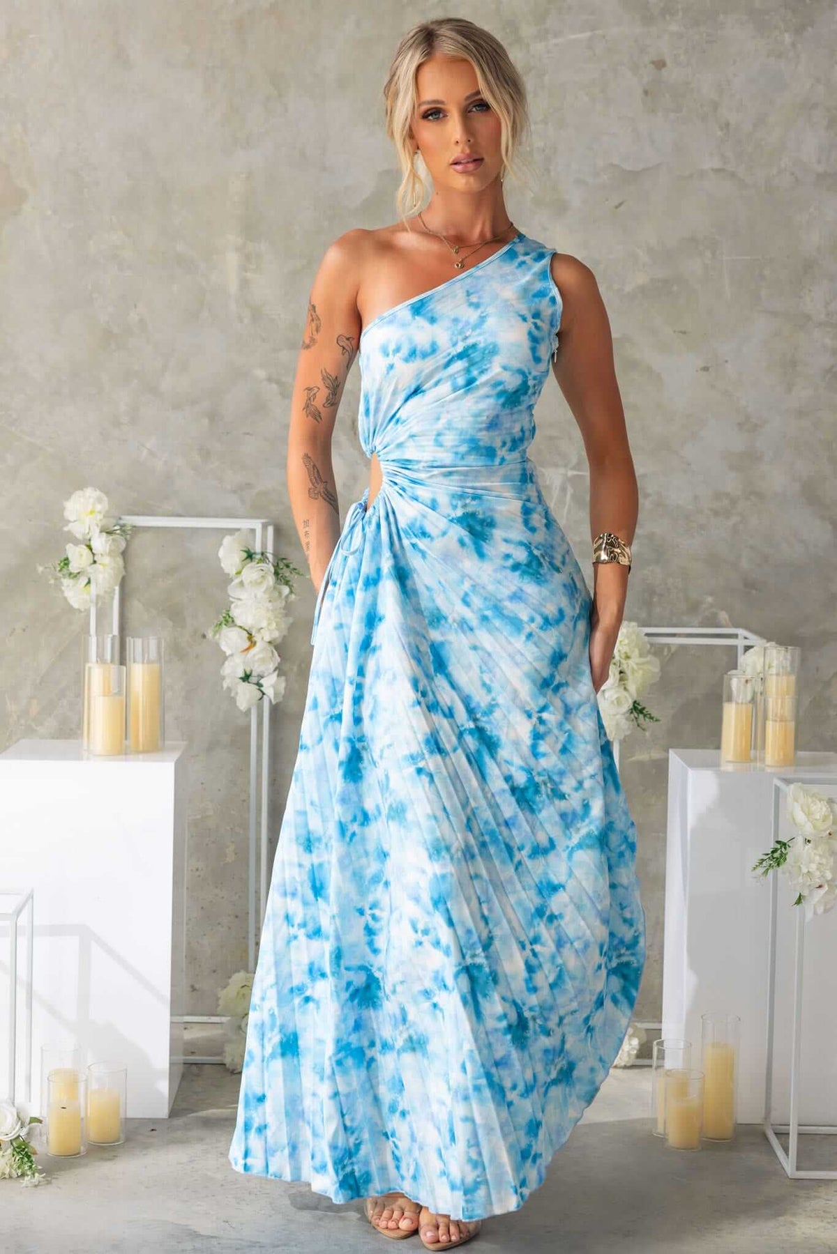 Tejano Maxi Dress featuring a one-shoulder design, cut-out waist, and flowy accordion pleat material in blue hues.