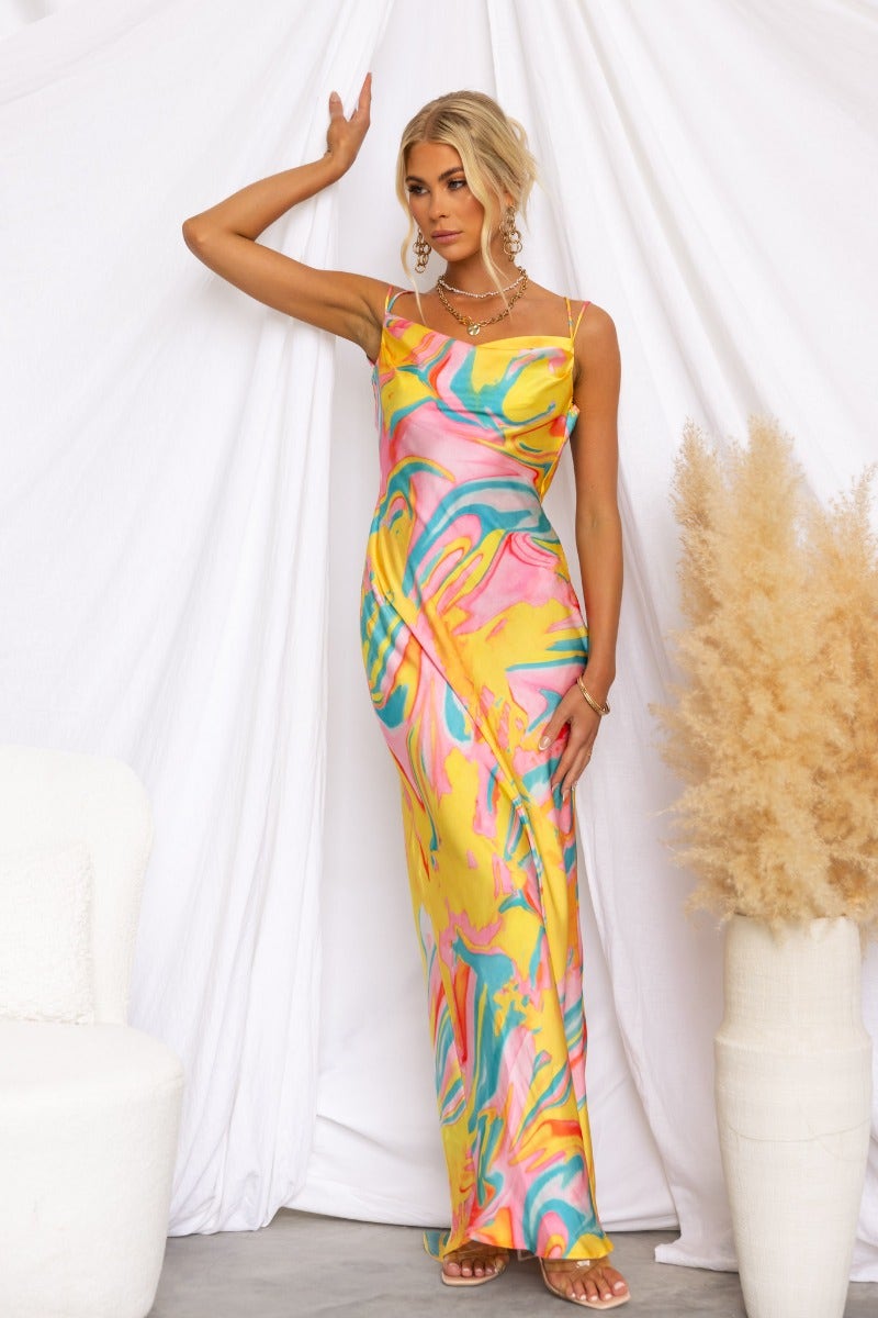 Model wearing a satin Visionary Maxi Dress with cowl neckline and colorful swirl pattern, set against a neutral backdrop.