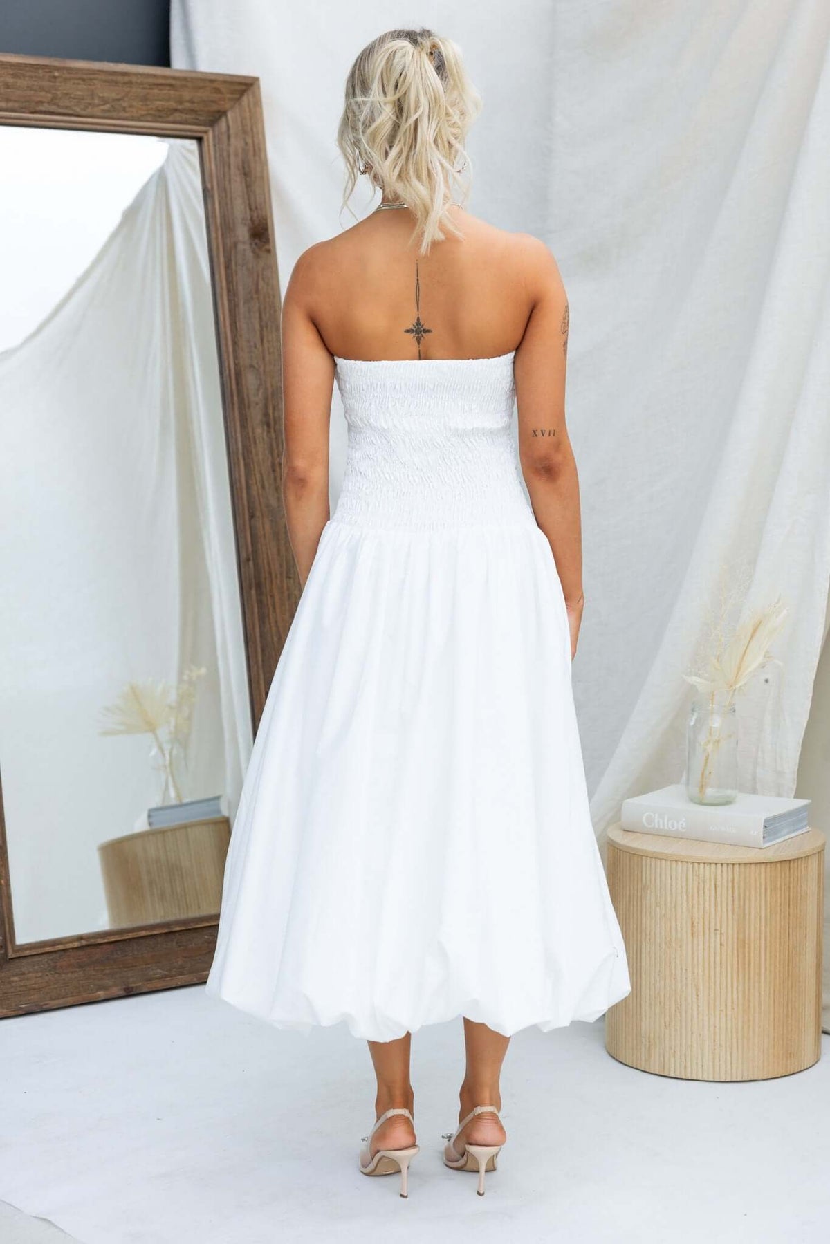 Back view of a strapless white midi dress with an elastic bodice, styled with a minimalist setting.