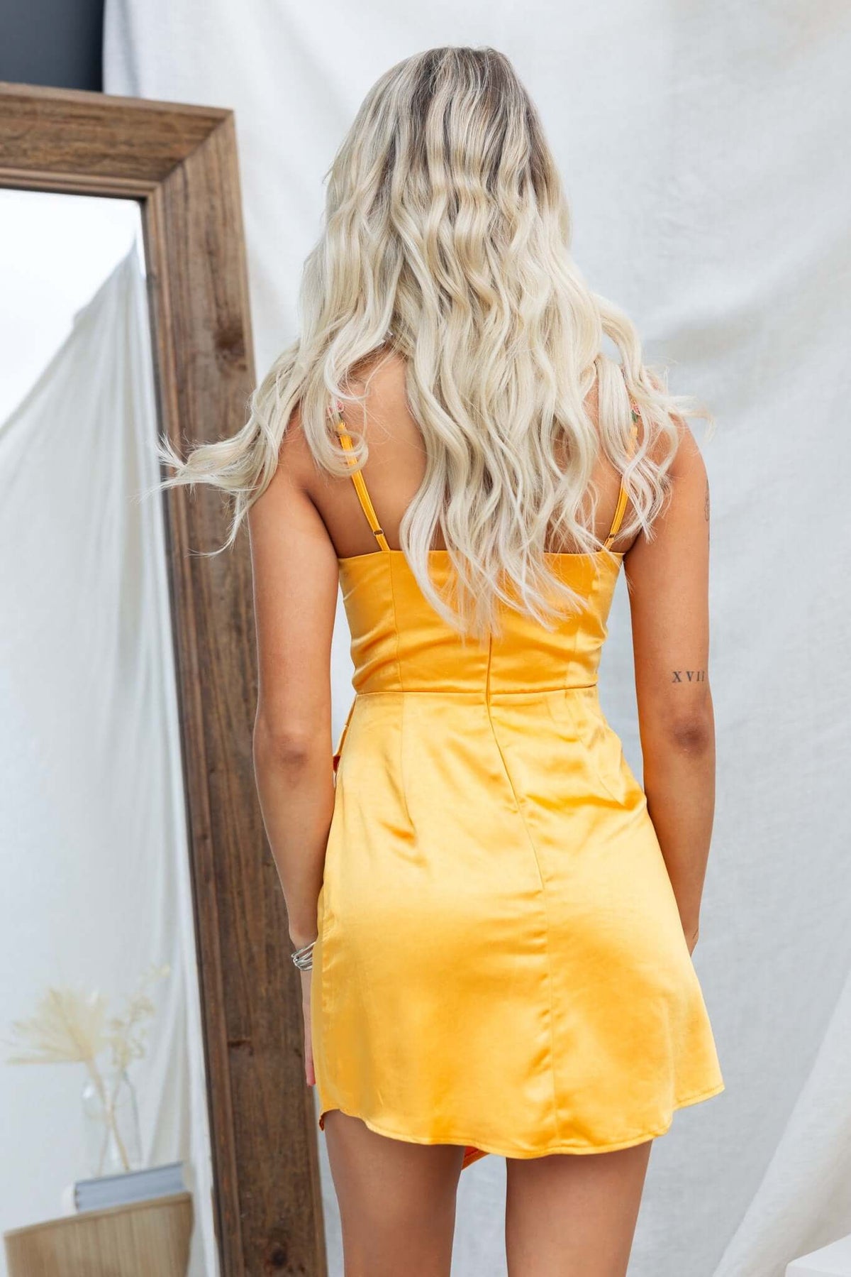 Back view of a model wearing a satin mini dress with adjustable straps and a floral trim.