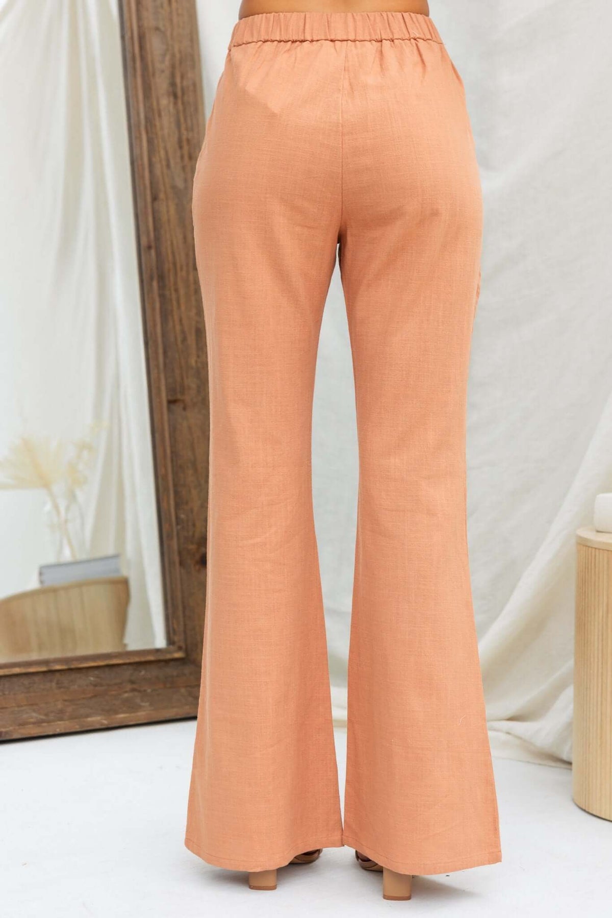 Back view of Stelline Pants in a soft orange color, featuring a mid-high waist and flared fit with an elastic back.