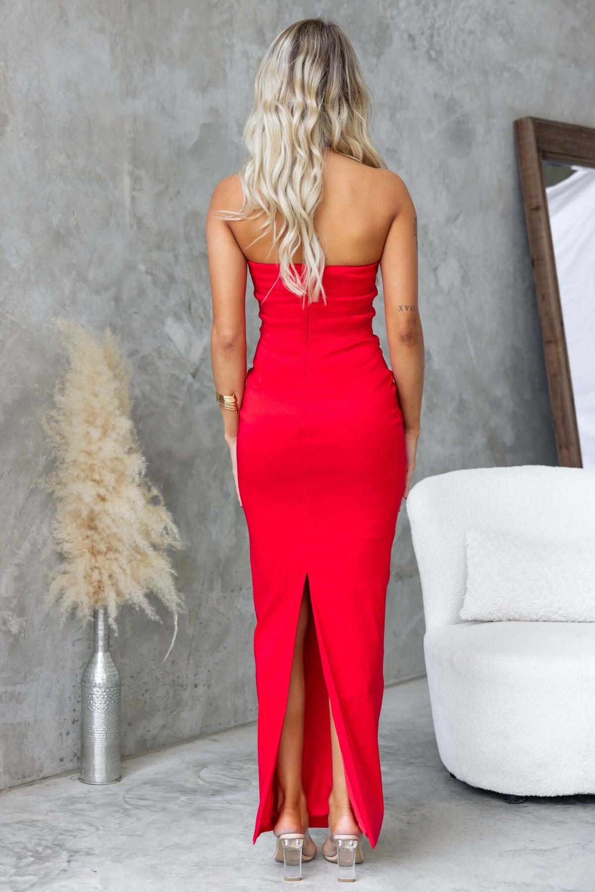 Rear view of a model wearing a red strapless Pontiac maxi dress with a back split and pleating, featuring a satin look.
