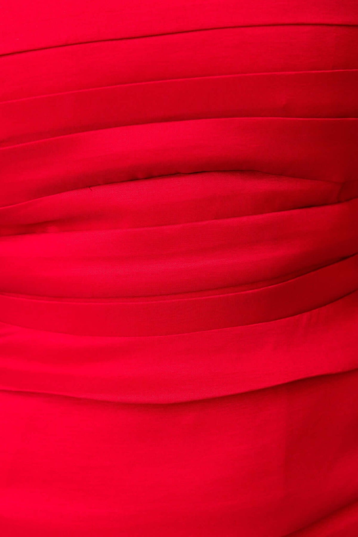 Close-up of red fabric with pleating detail on a strapless maxi dress, showcasing its satin look and texture.