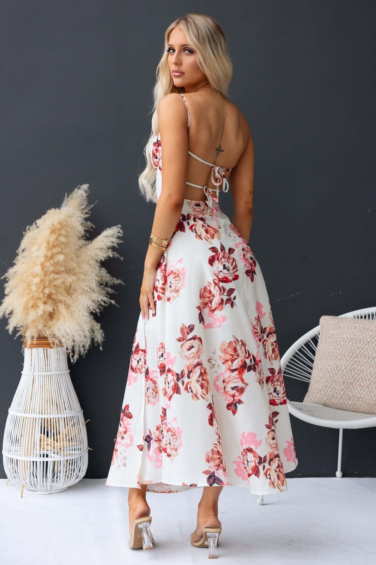 Back view of a woman in a floral midi dress with adjustable tie straps and a split, paired with stylish heels.