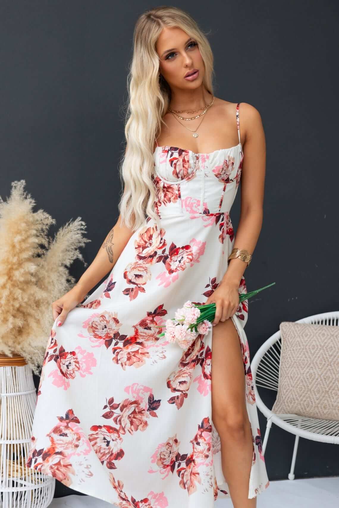 Woman in floral Burkes Midi Dress with adjustable tie straps, showing a front split and holding flowers.