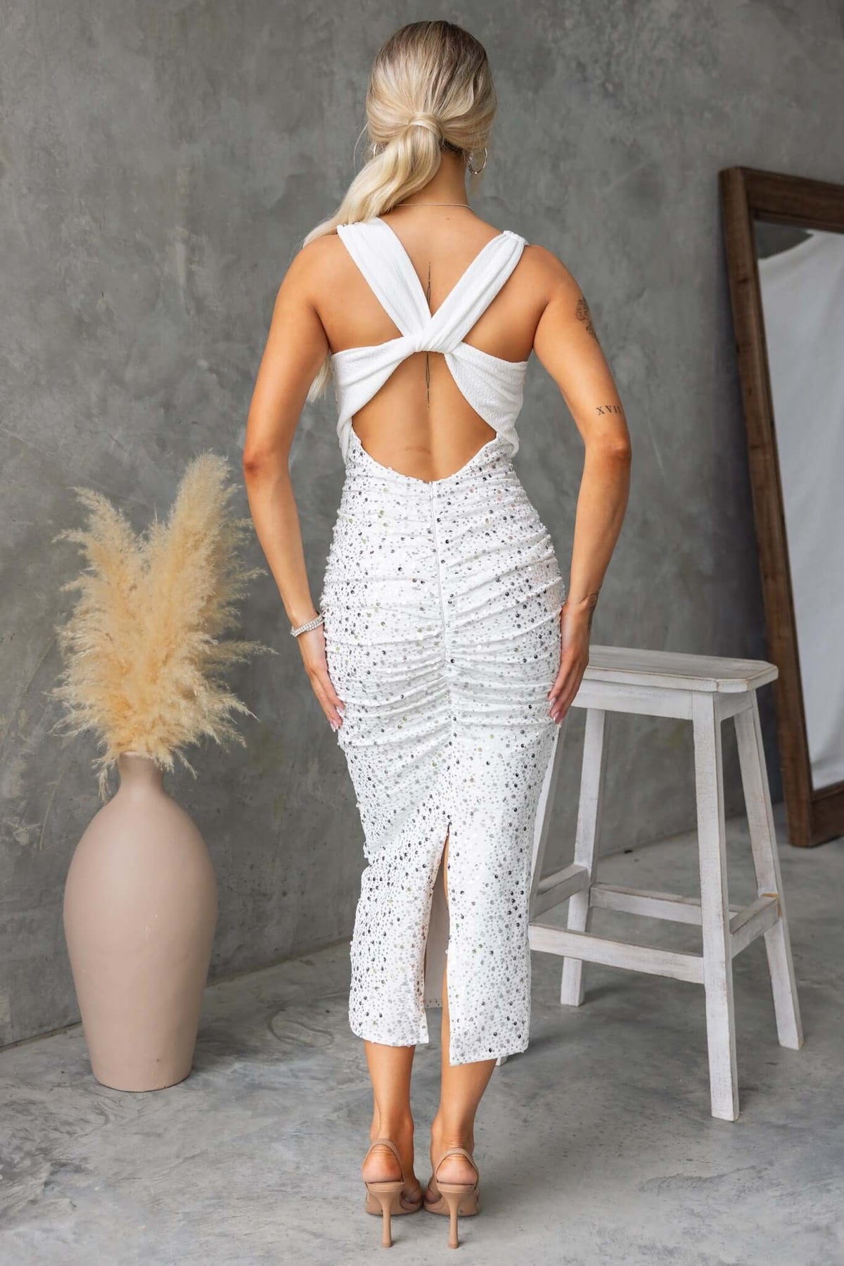 Elegant white maxi dress with sequins, cowl neckline, and open back, styled with a chic hairstyle.